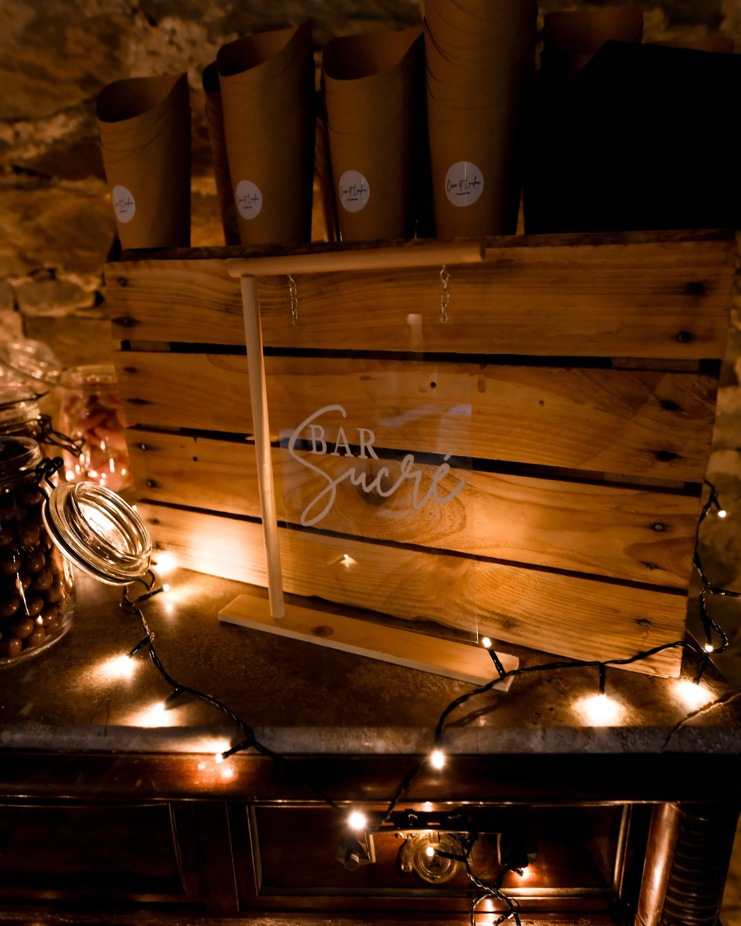 Vases en papier marron avec étiquettes blanches sur une étagère en bois, décorée de guirlandes lumineuses, dans une ambiance chaleureuse.