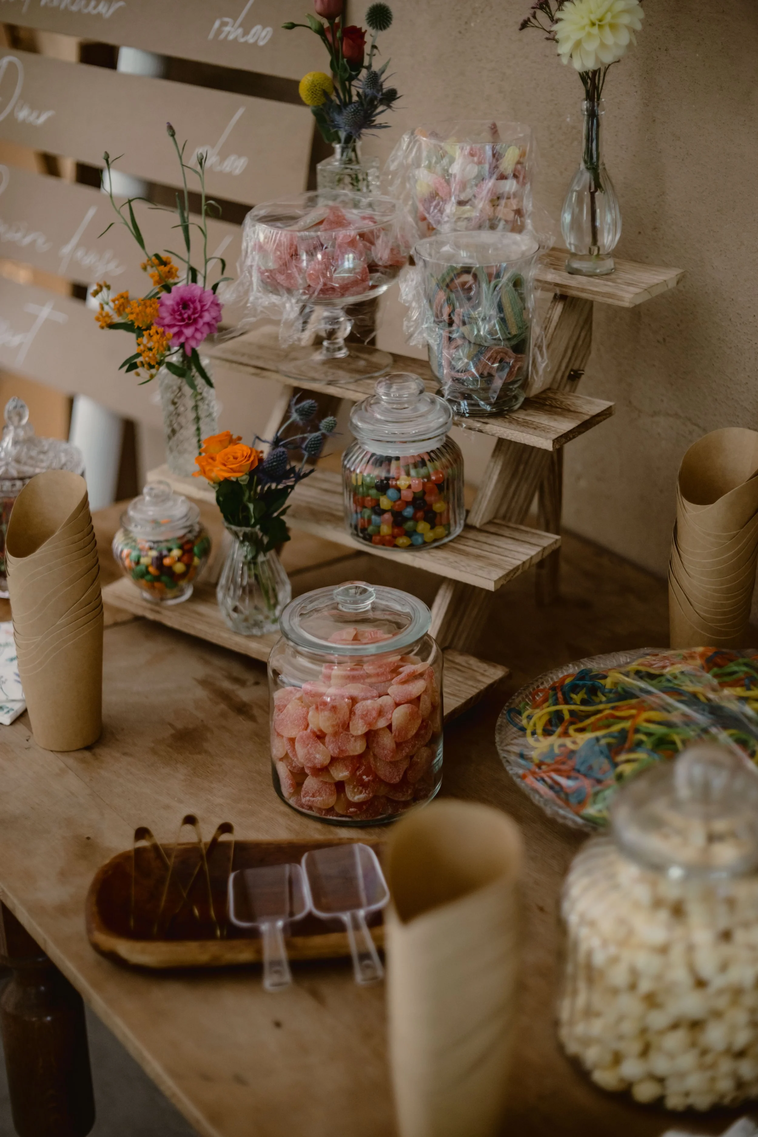 Présentoir de bonbons colorés dans des bocaux en verre, décorations florales avec fleurs sauvages, ambiance chaleureuse