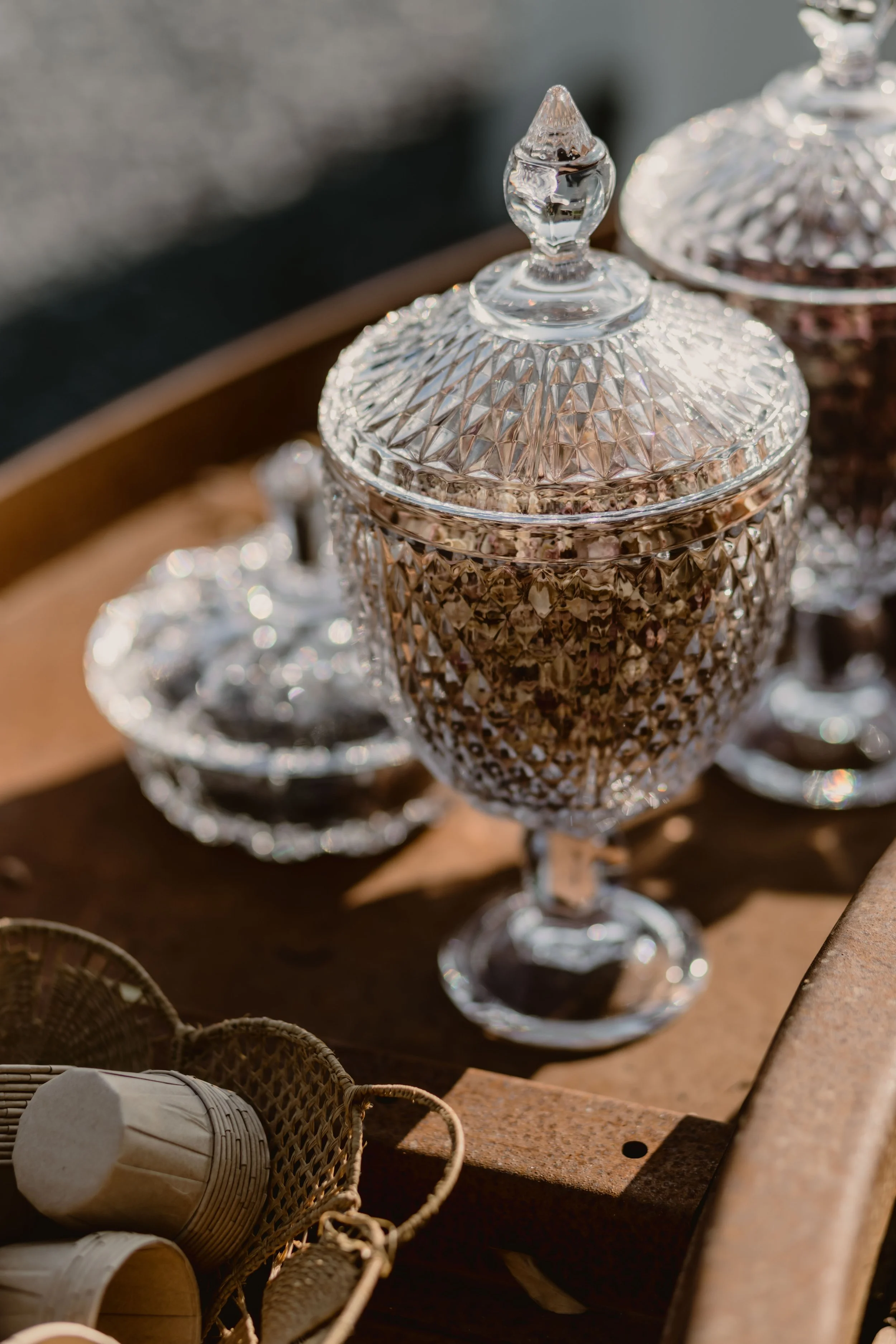 Verres en cristal avec couvercle, placé sur une table en bois, avec d'autres objets en arrière-plan.