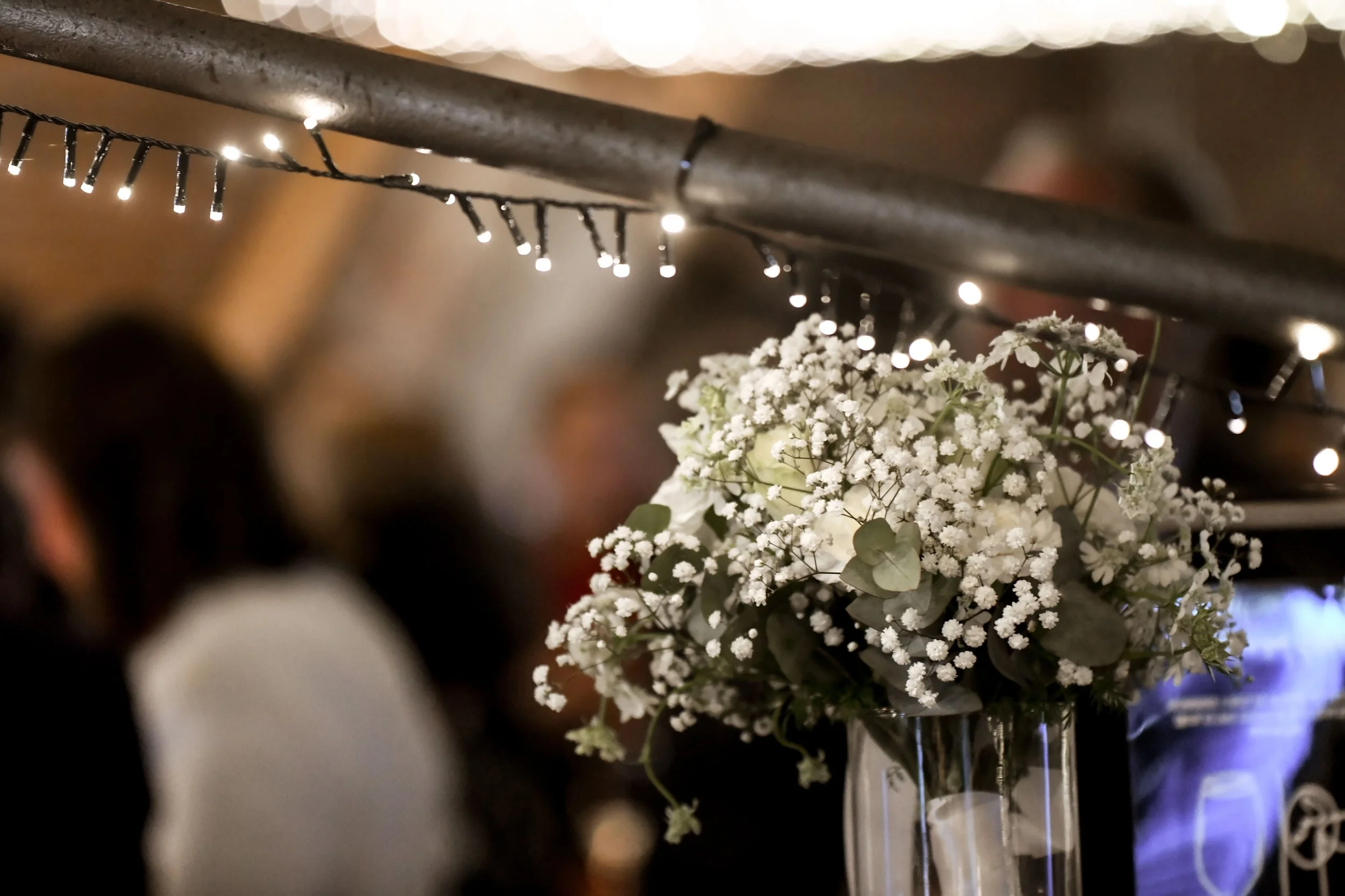 Un bouquet de fleurs blanches dans un vase en verre, avec de petites lumières en arrière-plan.