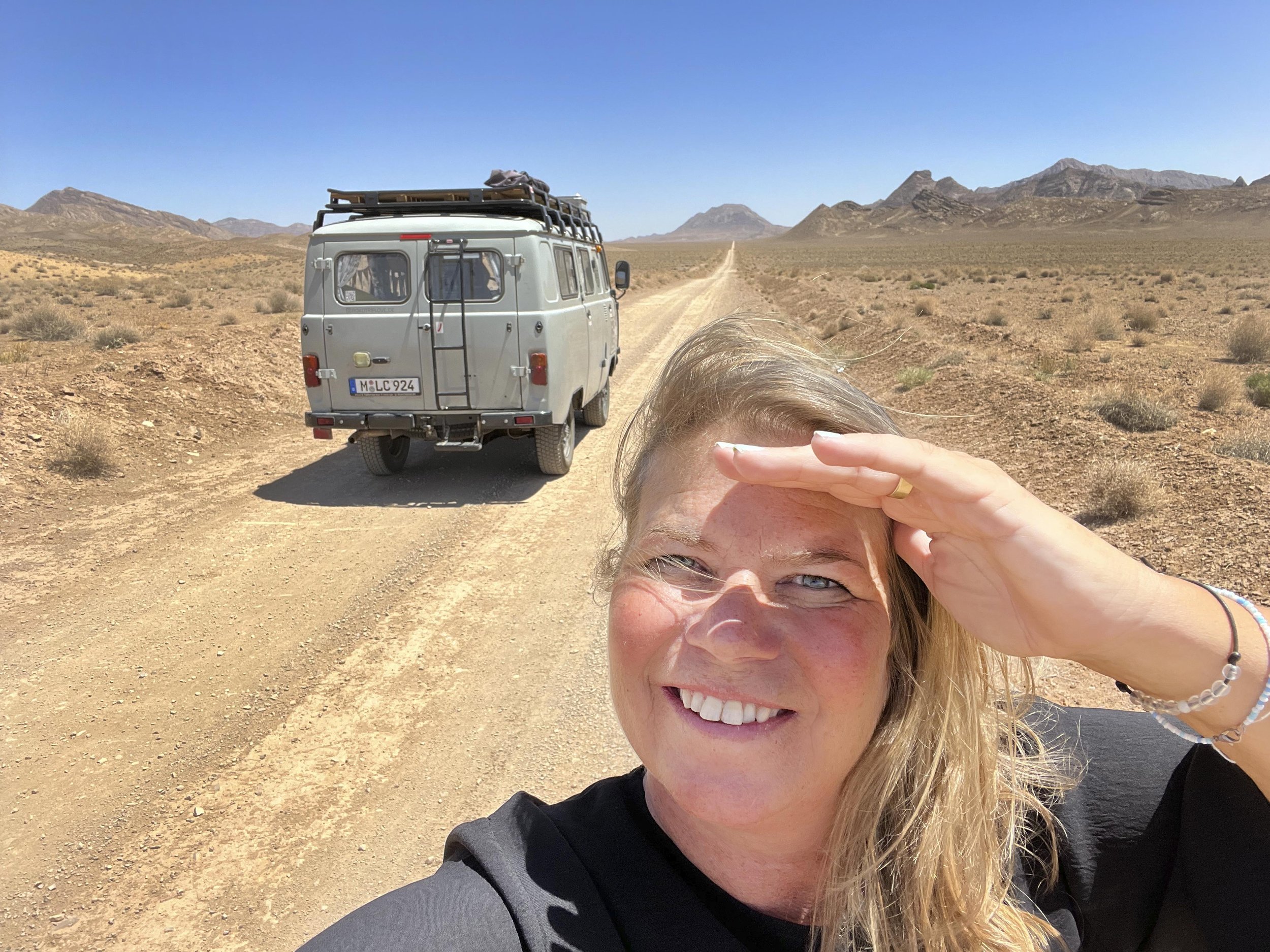 Eine Frau macht ein Selfie in der Wüste mit einem älteren Transporter im Hintergrund.