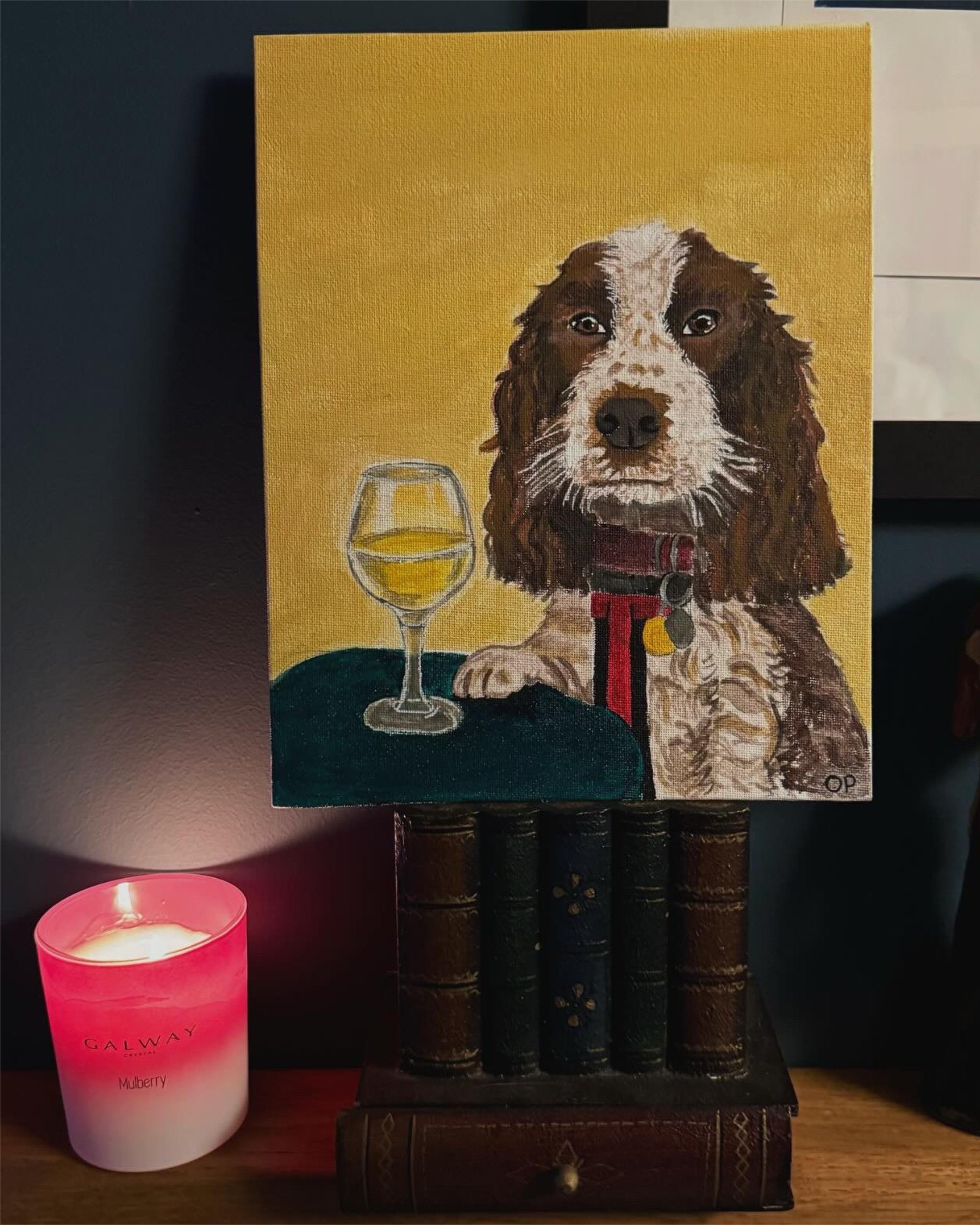 Painting of a brown and white dog with a red collar and a yellow tag, sitting next to a glass of white wine, on a small table with a drawer, with a yellow background.
