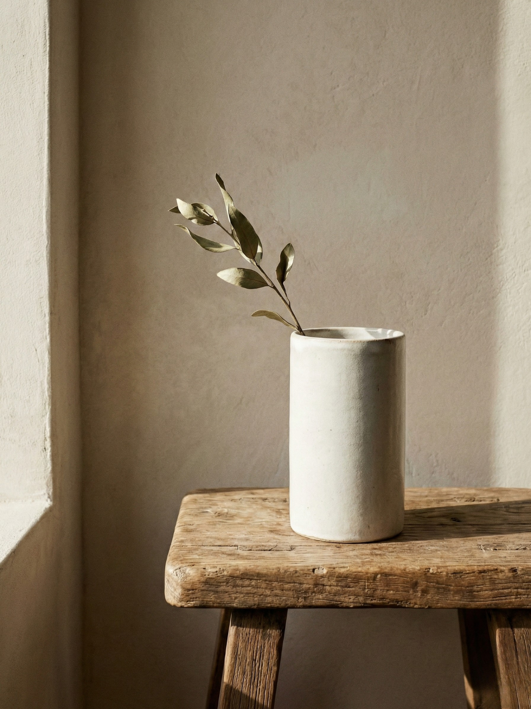 vignette of a wood bench with a ceramic vase and an olive branch