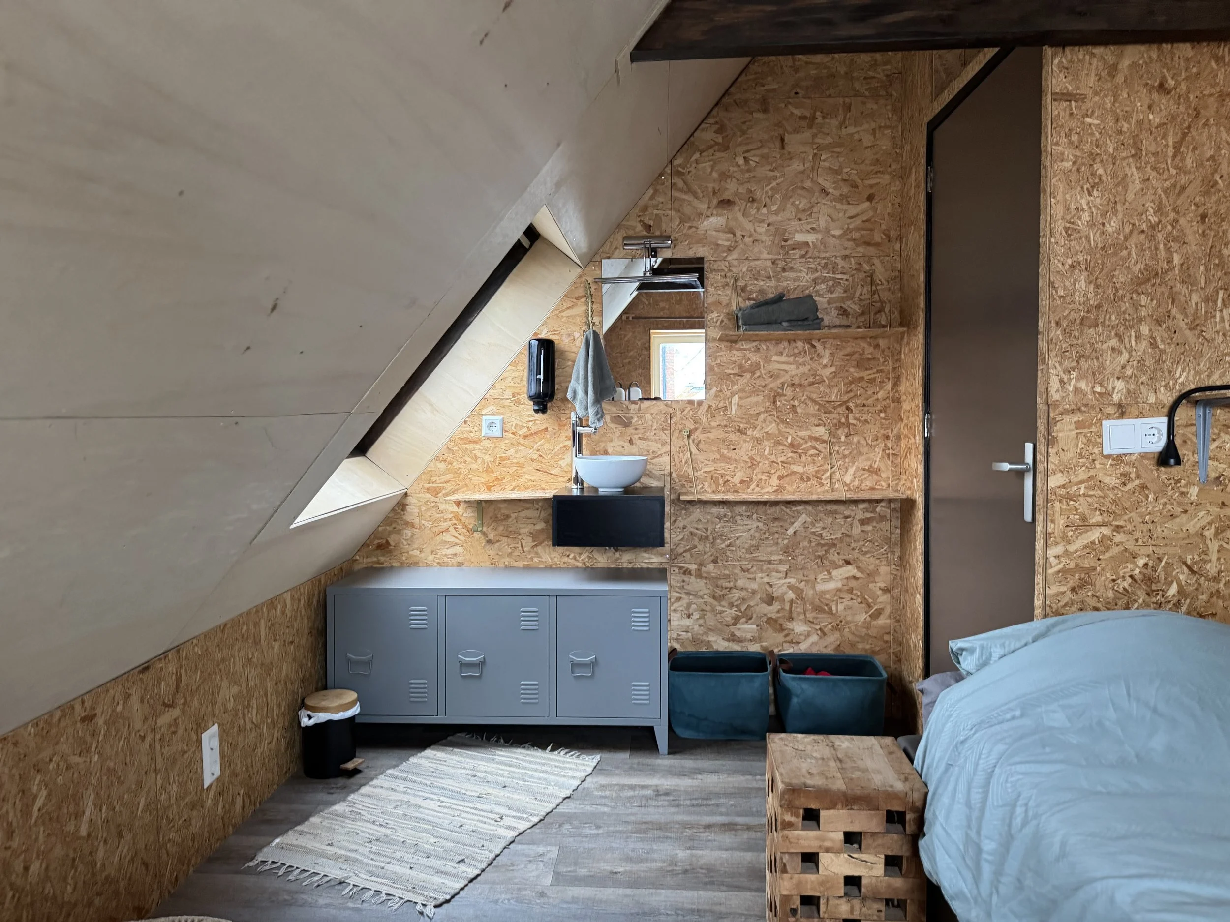 Sfeervolle slaapkamer in de B&B met twee eenpersoonsbedden, schuine wanden en natuurlijke materialen, rustig ingericht met wastafelmeubel en praktische opbergruimte.