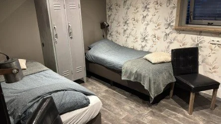 Rustig ingerichte slaapkamer in de B&B met twee eenpersoonsbedden, praktische kastruimte en zitstoel, ideaal voor een comfortabele overnachting in een sfeervolle kamer.