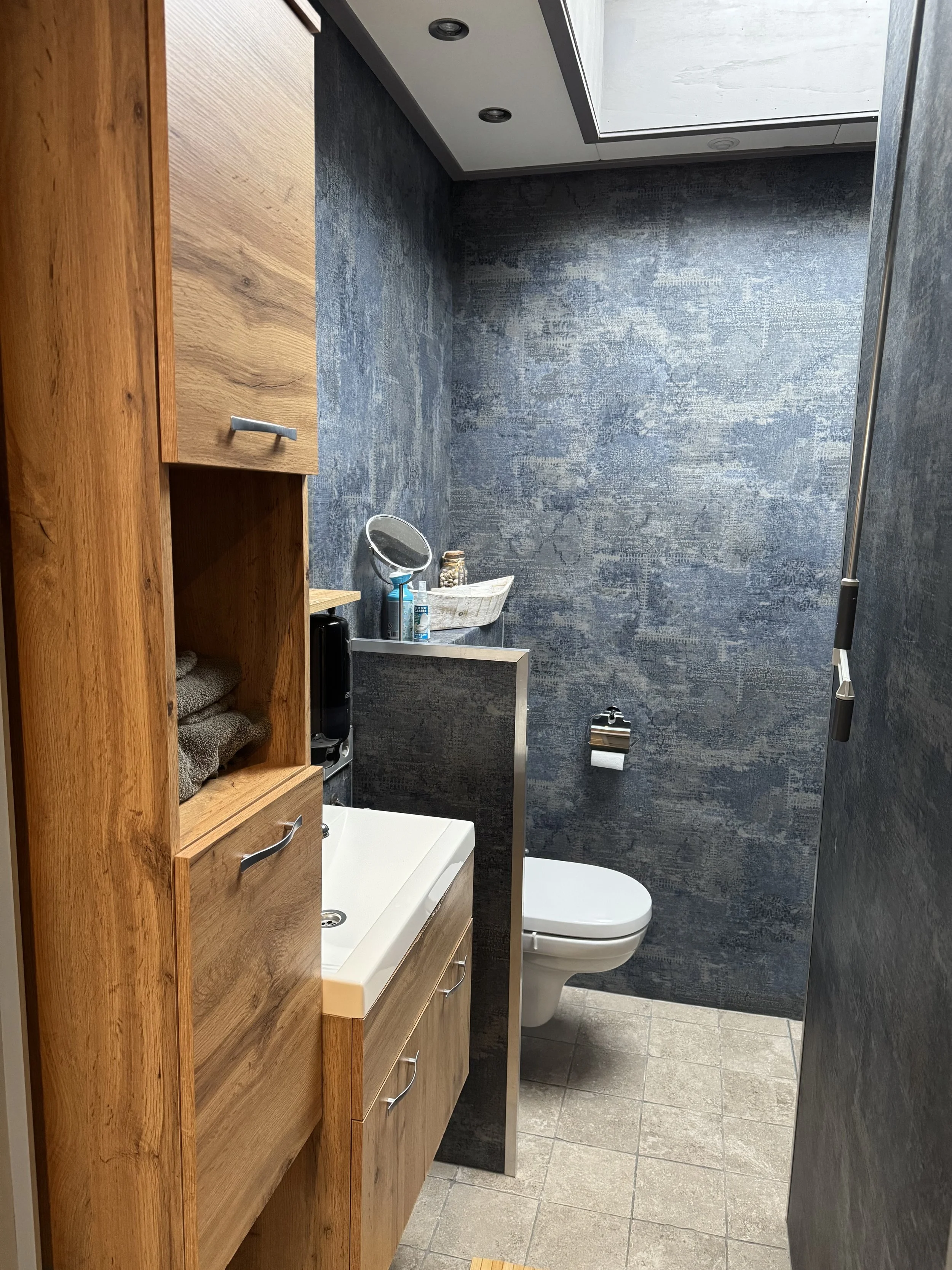 Moderne compacte badkamer bij de kamer in de B&B met douche en toilet, strak afgewerkt met donkere kleur, wastafelmeubel en dakraam voor natuurlijk licht.