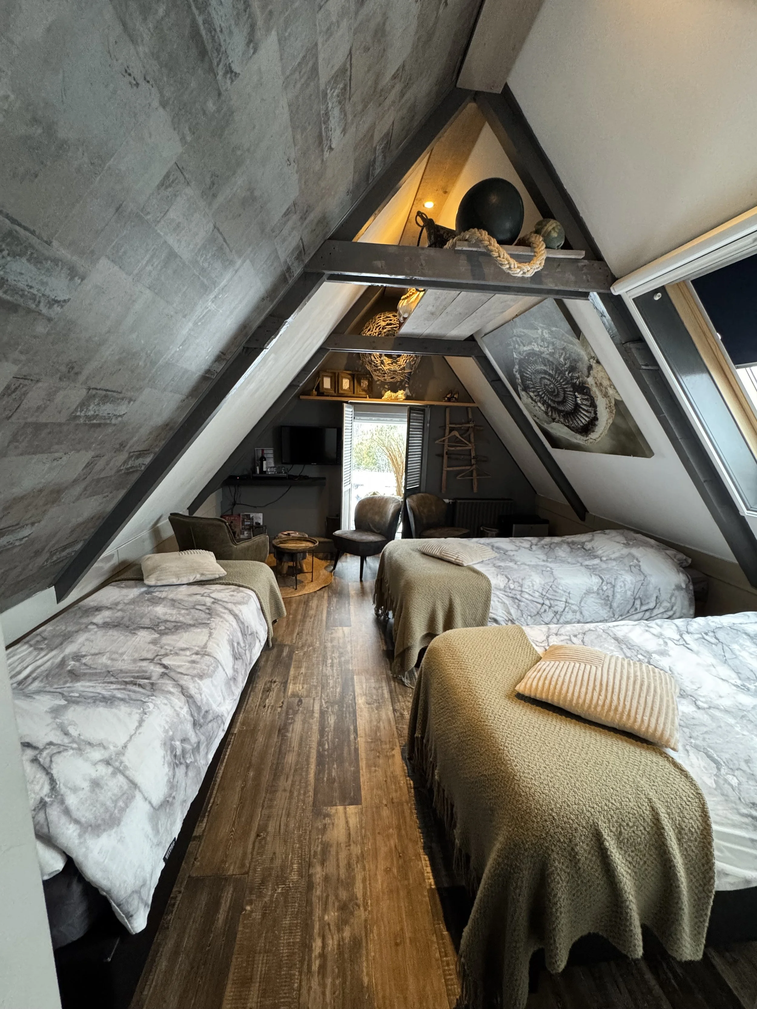 Ruime 3-persoonskamer op de bovenverdieping van de B&B met drie eenpersoonsbedden, houten vloer en schuine wanden, sfeervol ingericht met warme materialen en natuurlijk licht.