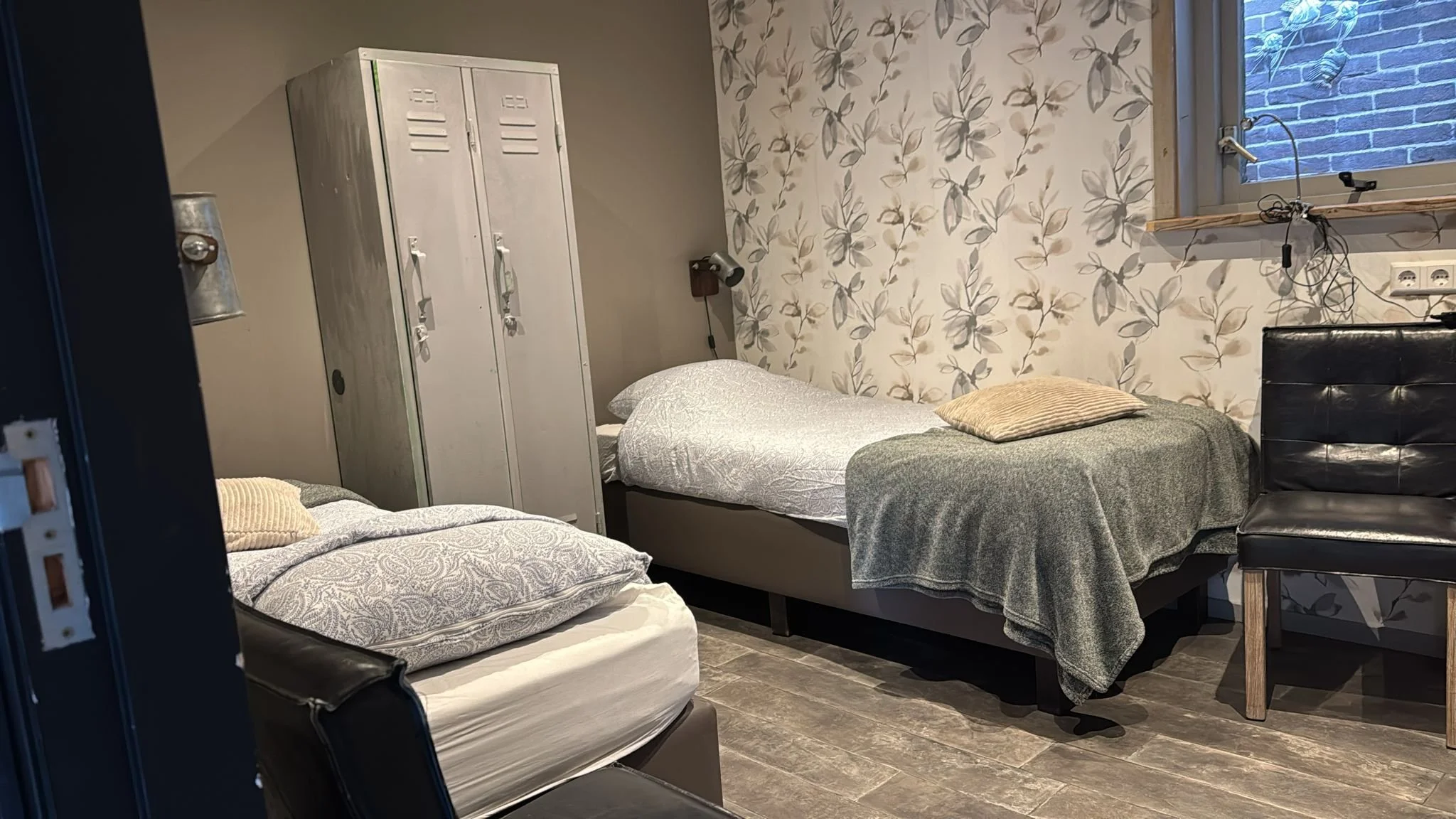 een foto van de beneden slaapkamer van het appartement met twee bedden een stoel en een grijze kast.