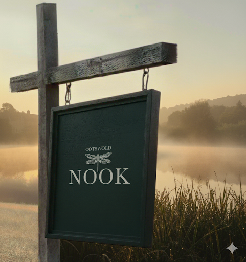 A sign hanging from a wooden post by a lake at sunrise, reading "Cotswold Nook."
