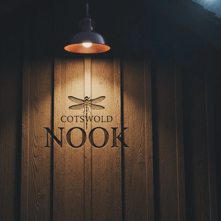 Wooden sign with a dragonfly illustration and the words 'Cotswold Nook' illuminated by a hanging light.