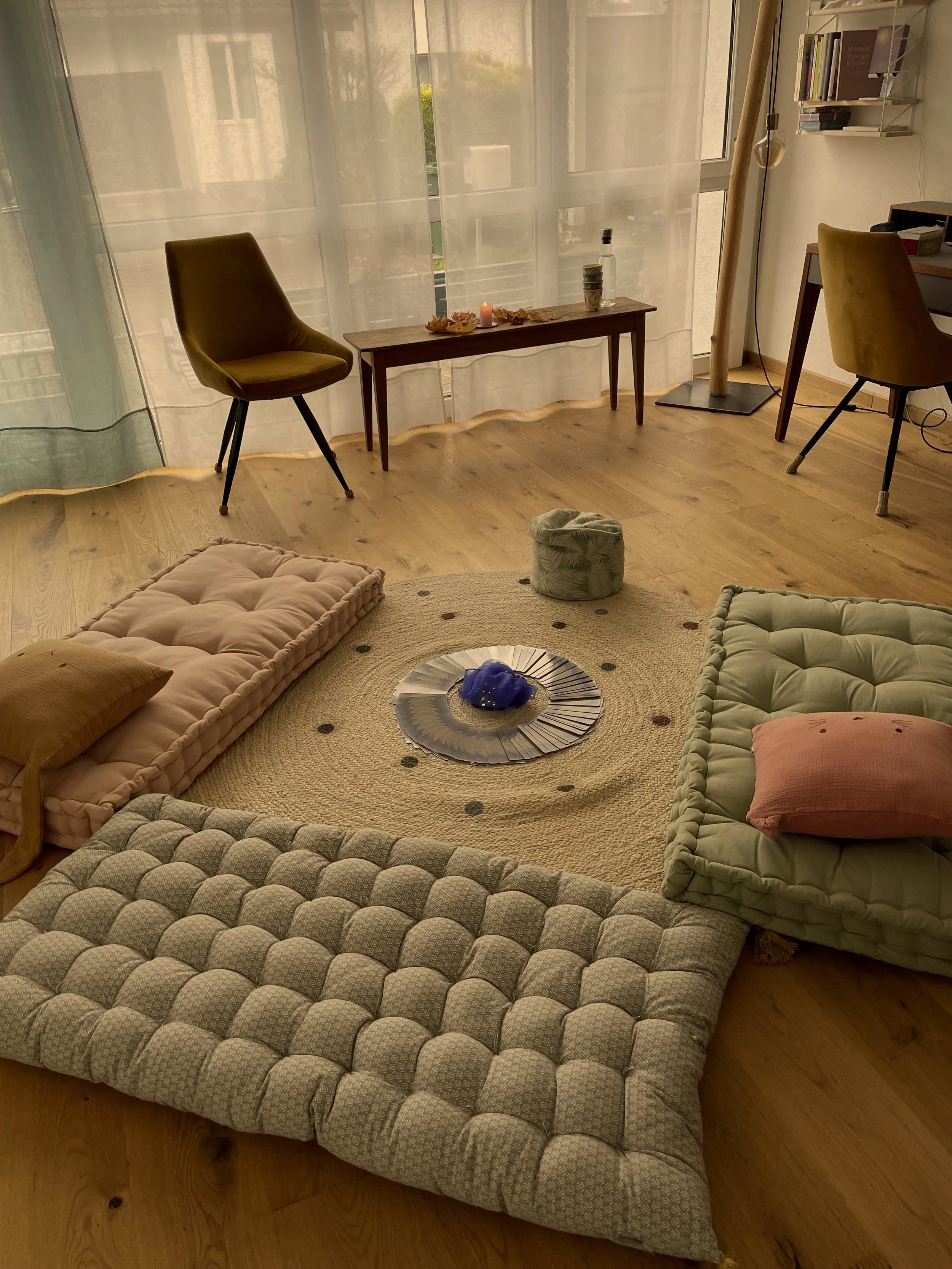 Gemütliches Wohnzimmer mit Tatami-Matten, Kissen, einem runden Teppich, einem Glas Teller, und einem Raum mit großem Fenster und Holzboden.