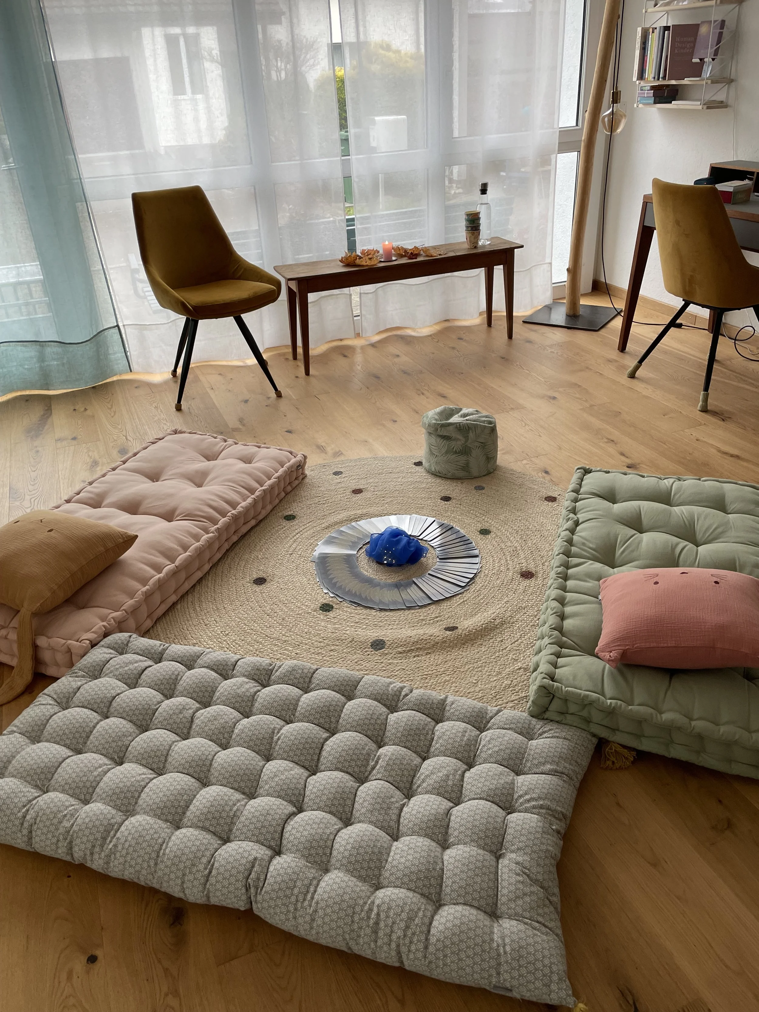 Gemütliches Wohnzimmer mit Tatami-Matten, Kissen, einem runden Teppich, einem Glas Teller, und einem Raum mit großem Fenster und Holzboden.