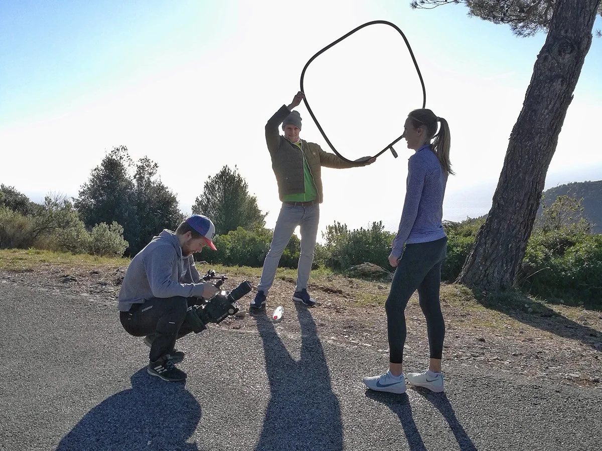 Drei Personen im Freien bei einem Fotoshooting. Eine Person hält eine Kamera, eine andere einen Reflektor und eine Frau posiert.