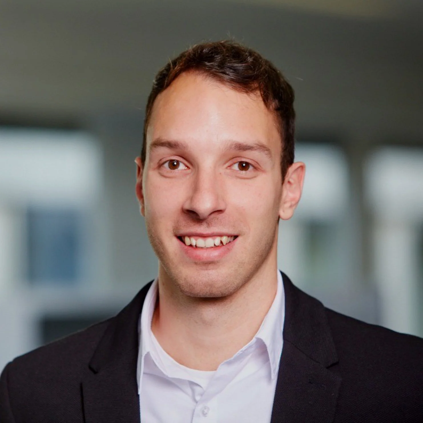 Porträt eines lächelnden Mannes im Anzug vor unscharfem Hintergrund.