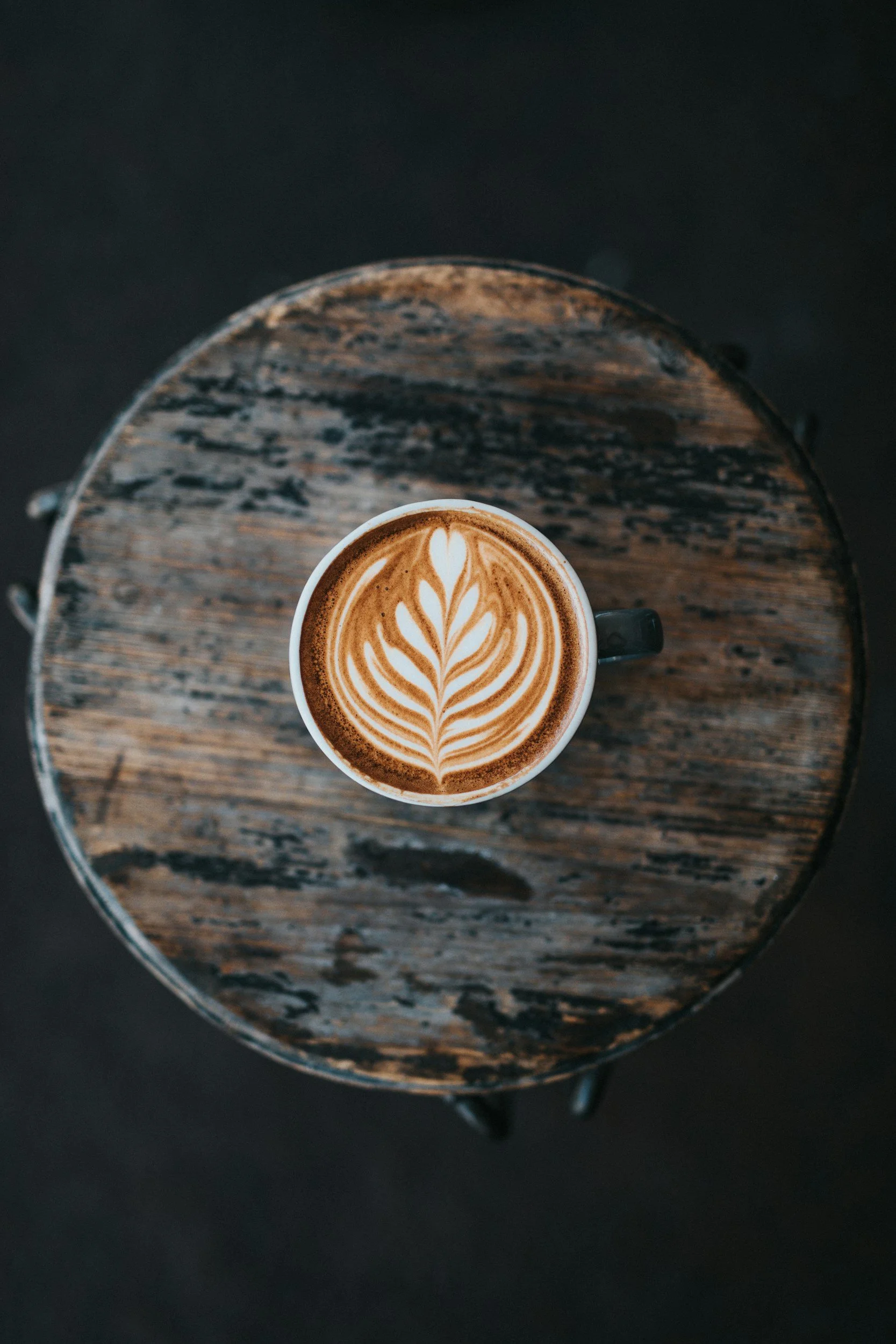 A top-down view of a latte with latte art on a distressed wooden table.
