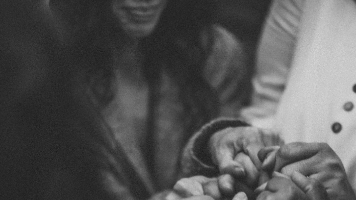 Close-up of two people holding hands, with one person's hand gently grasping the other's.