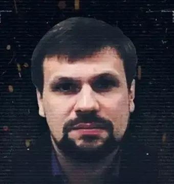 A man with dark hair, facial hair, and a serious expression, wearing a dark-colored shirt, standing outdoors at night.