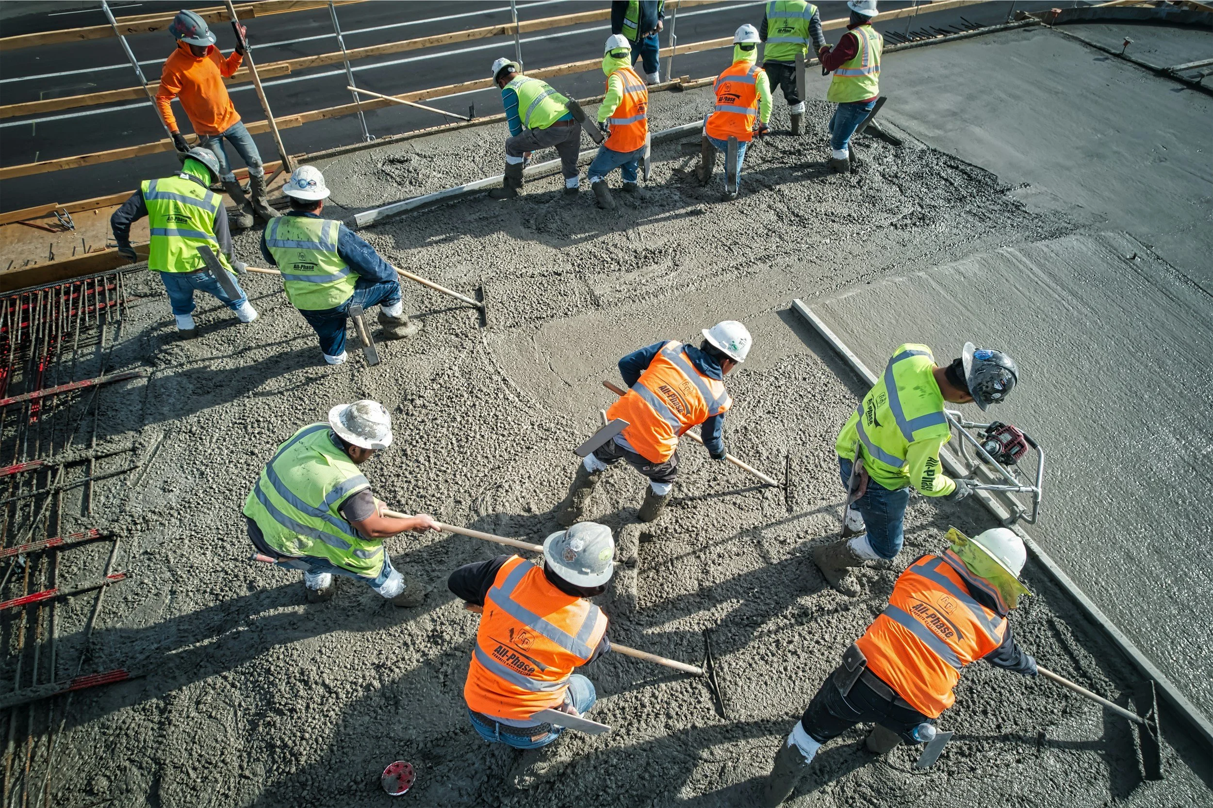 Construction workers in safety vests and helmets pouring and spreading concrete on a building site.