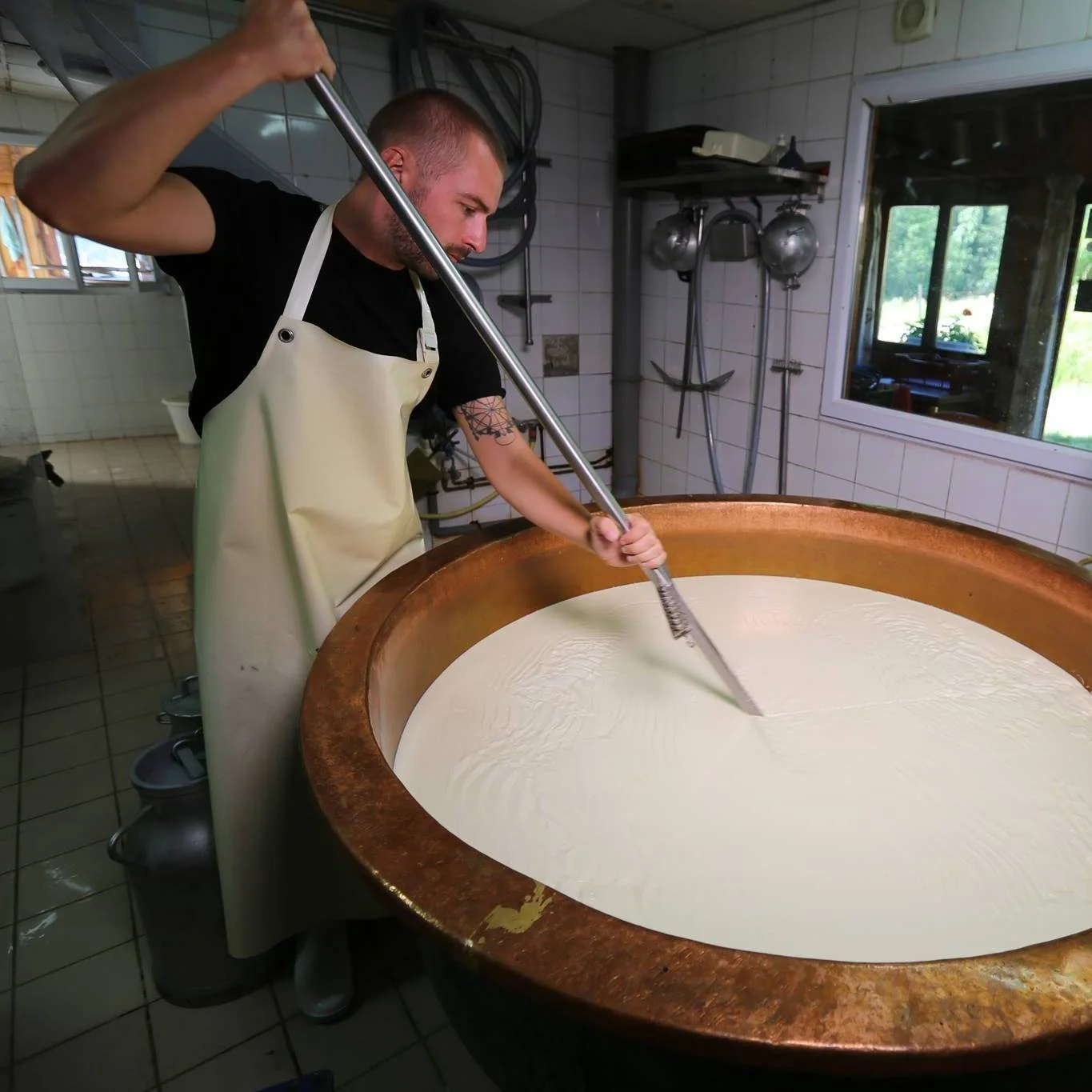 Un homme remue du lait dans un grand chaudron en cuivre, dans une cuisine