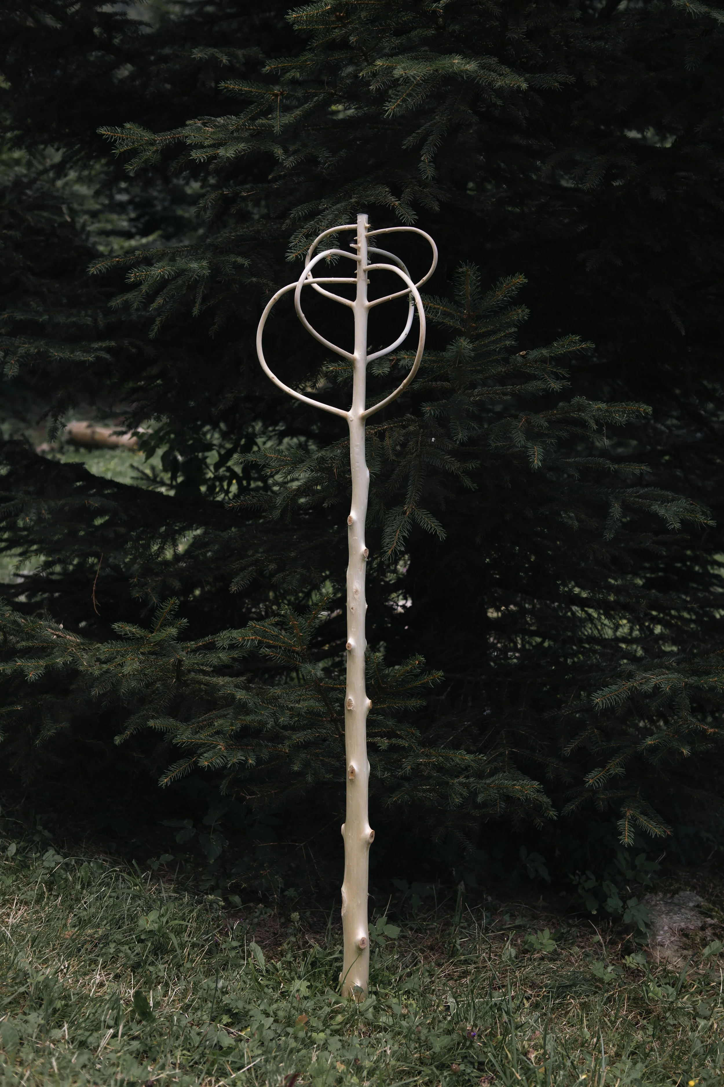 Un arbre décoratif en forme de lance-flammes, posé sur un terrain herbeux avec un arrière-plan de sapin.