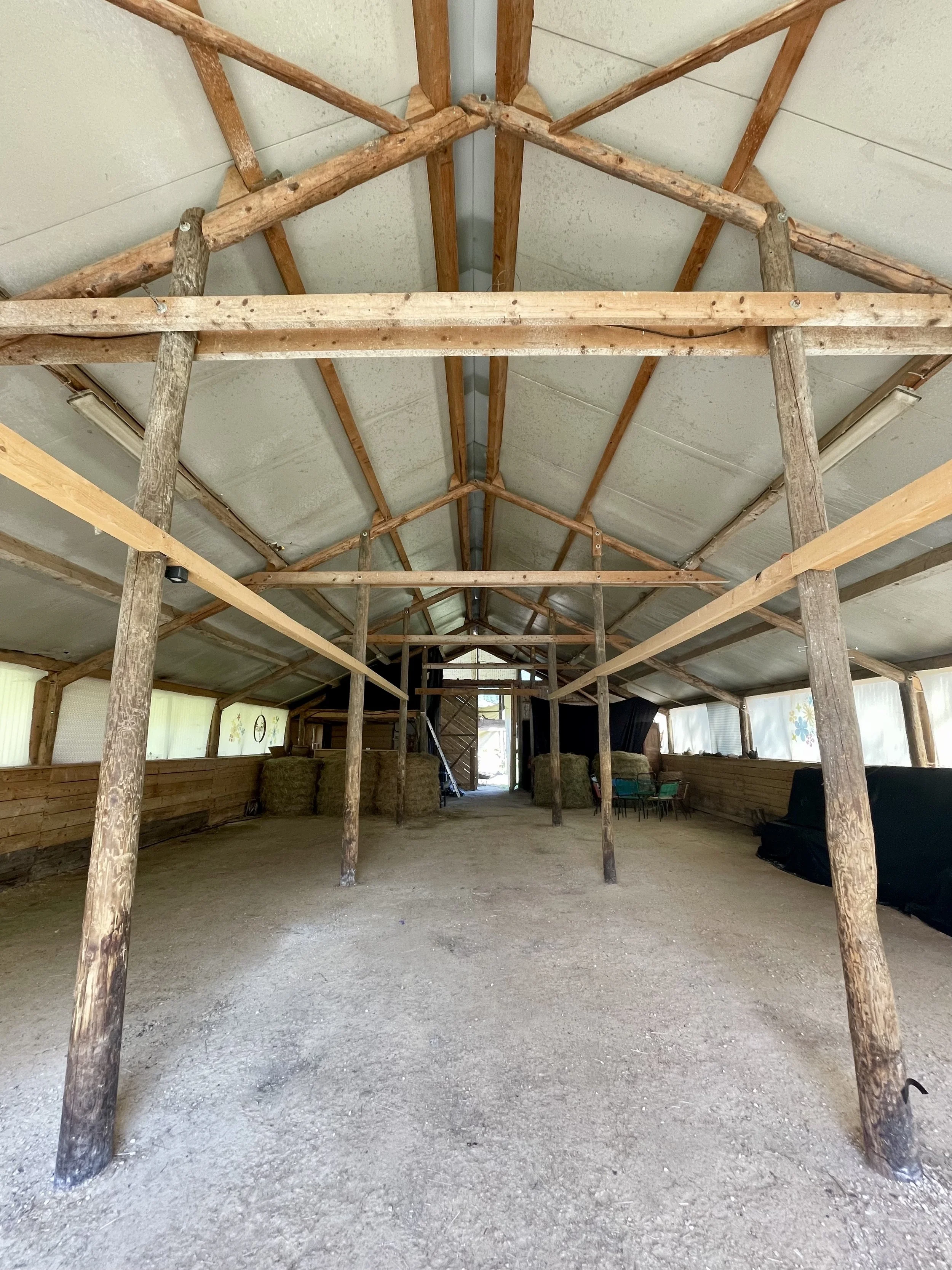 L'intérieur d'une ferme ou d'une grange avec une structure en bois, une toiture en toile, et des balles de foin, sans présence humaine.