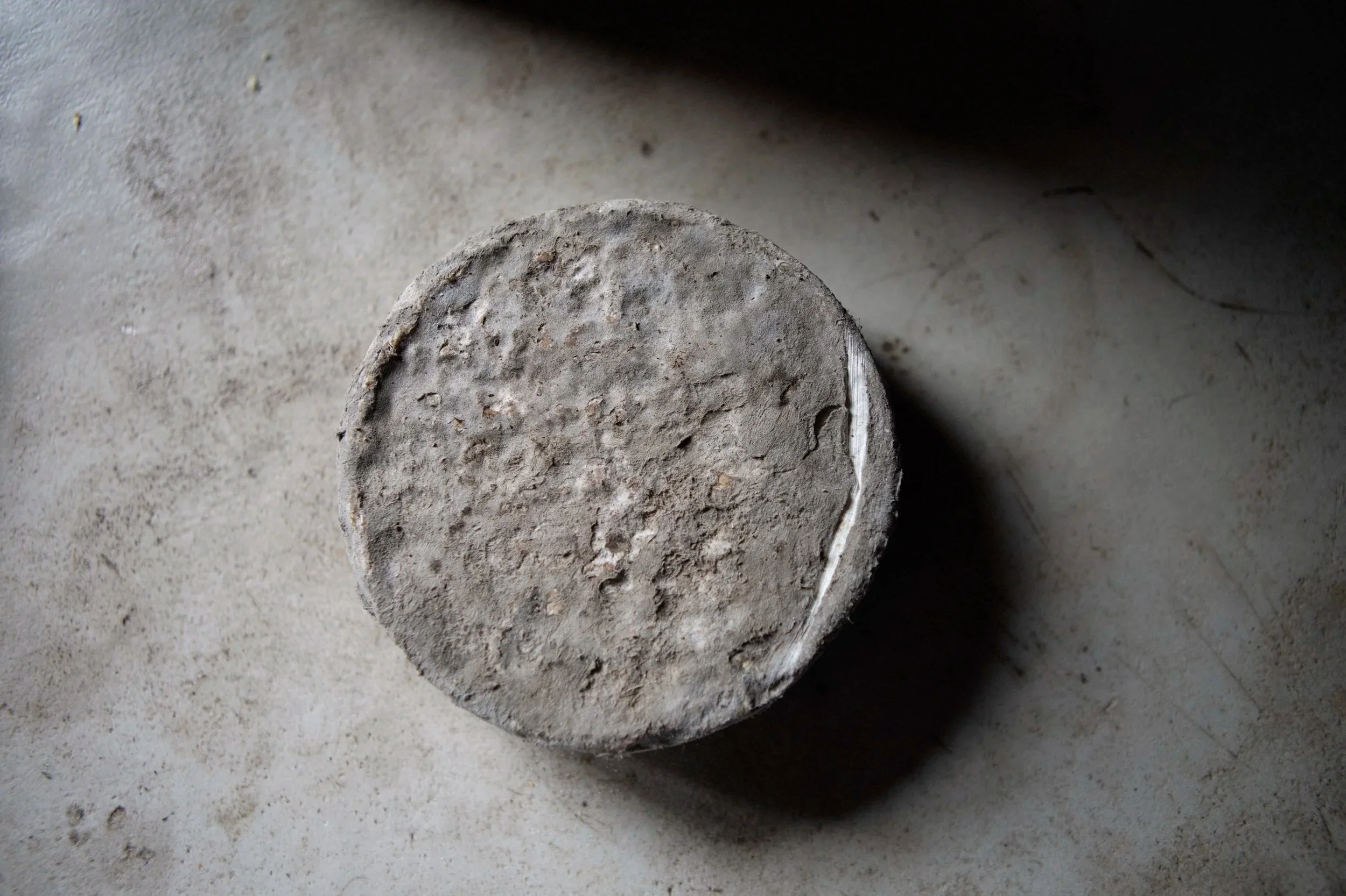 Un objet circulaire en béton ou en pierre poussiéreux posé sur une surface grise, vu d'en haut.