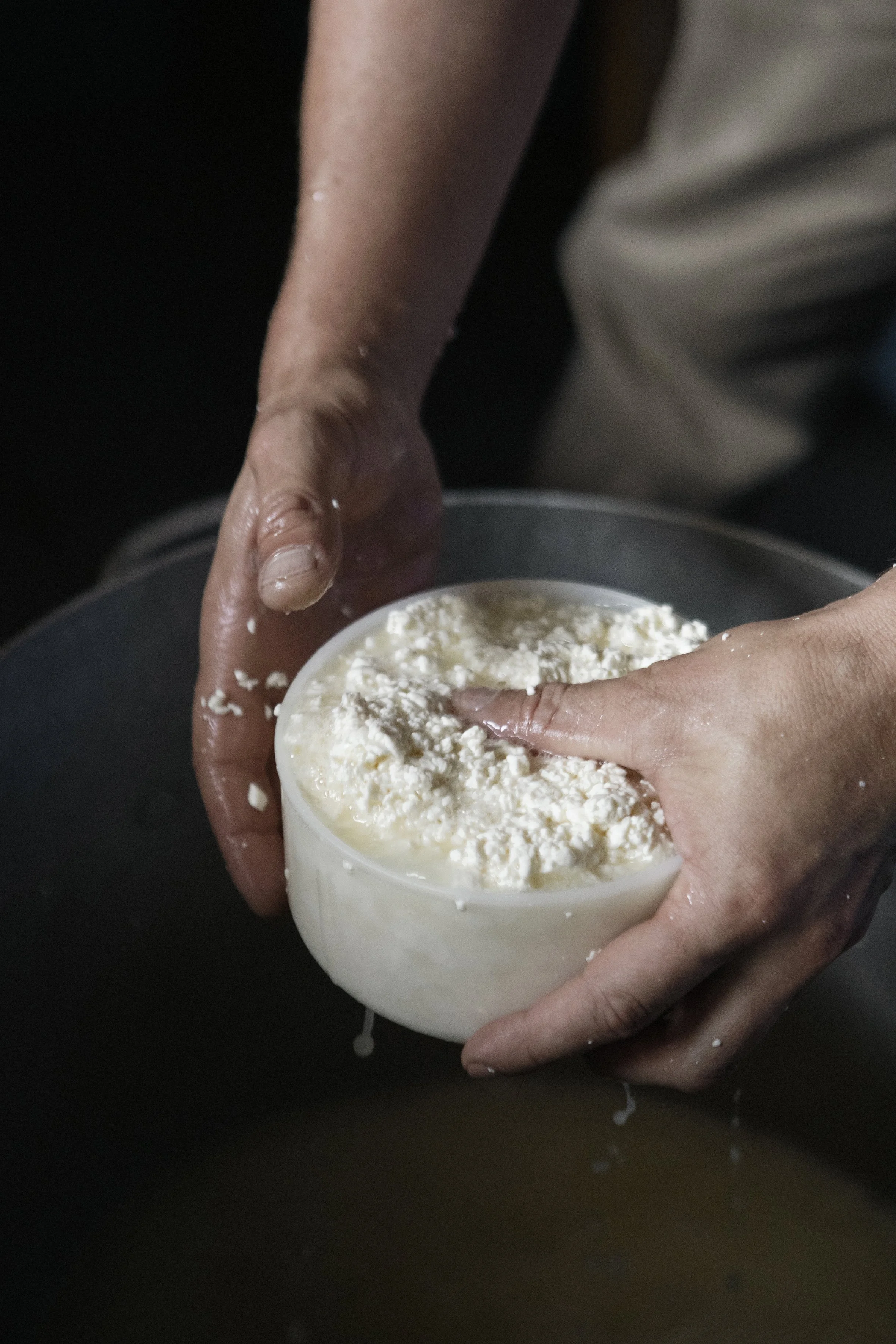 Personnes manipulant du fromage frais placé dans un bol blanc.