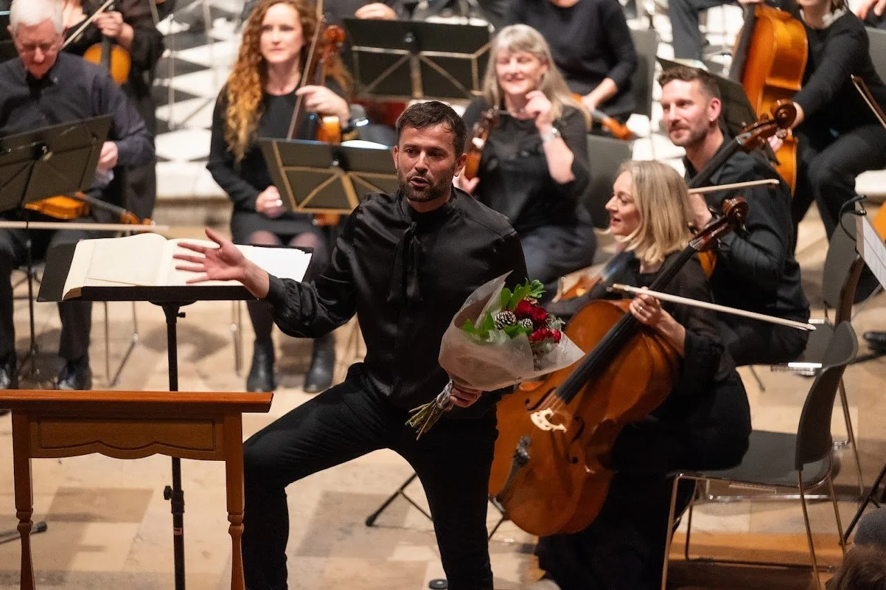 Conductor holding a bouquet of flowers in front of an orchestra during a performance.
