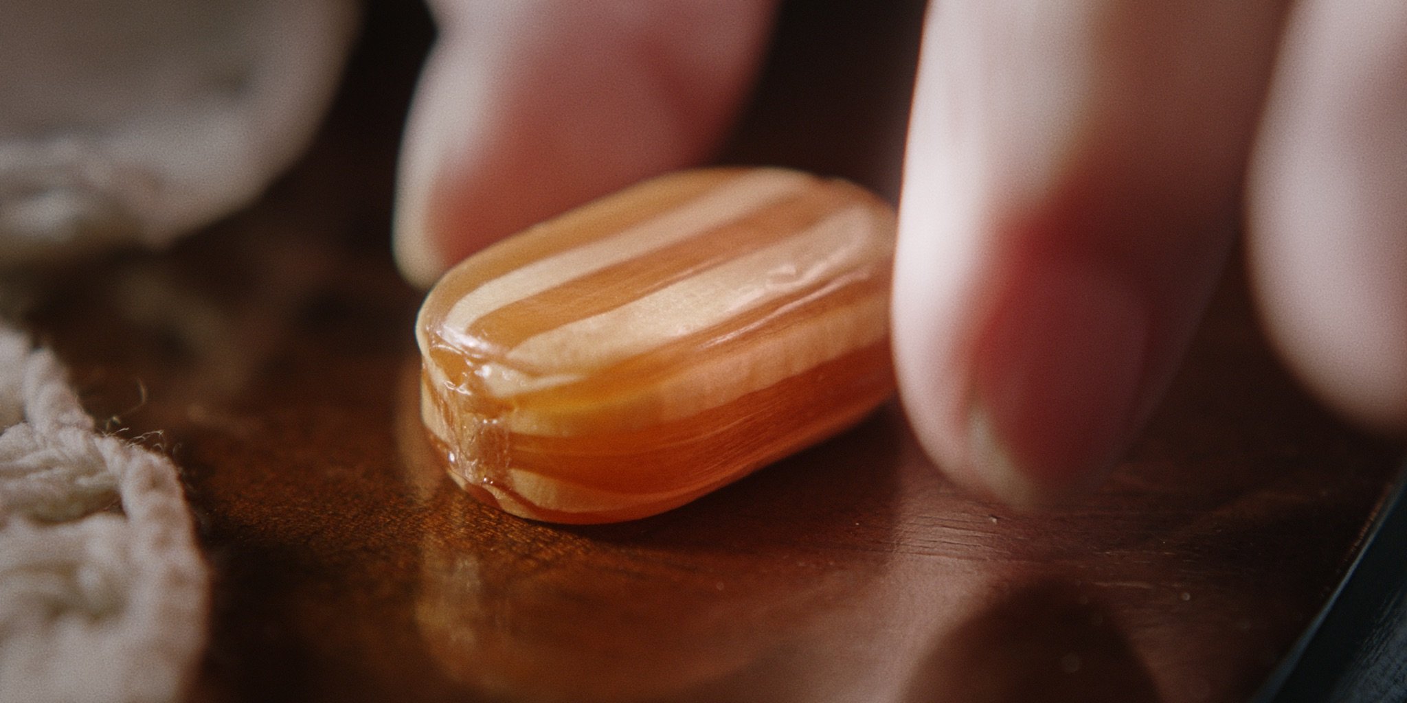 Close-up of a striped, rectangular candy (a mint humbug) with caramel and cream-colored stripes, resting on a wooden surface.