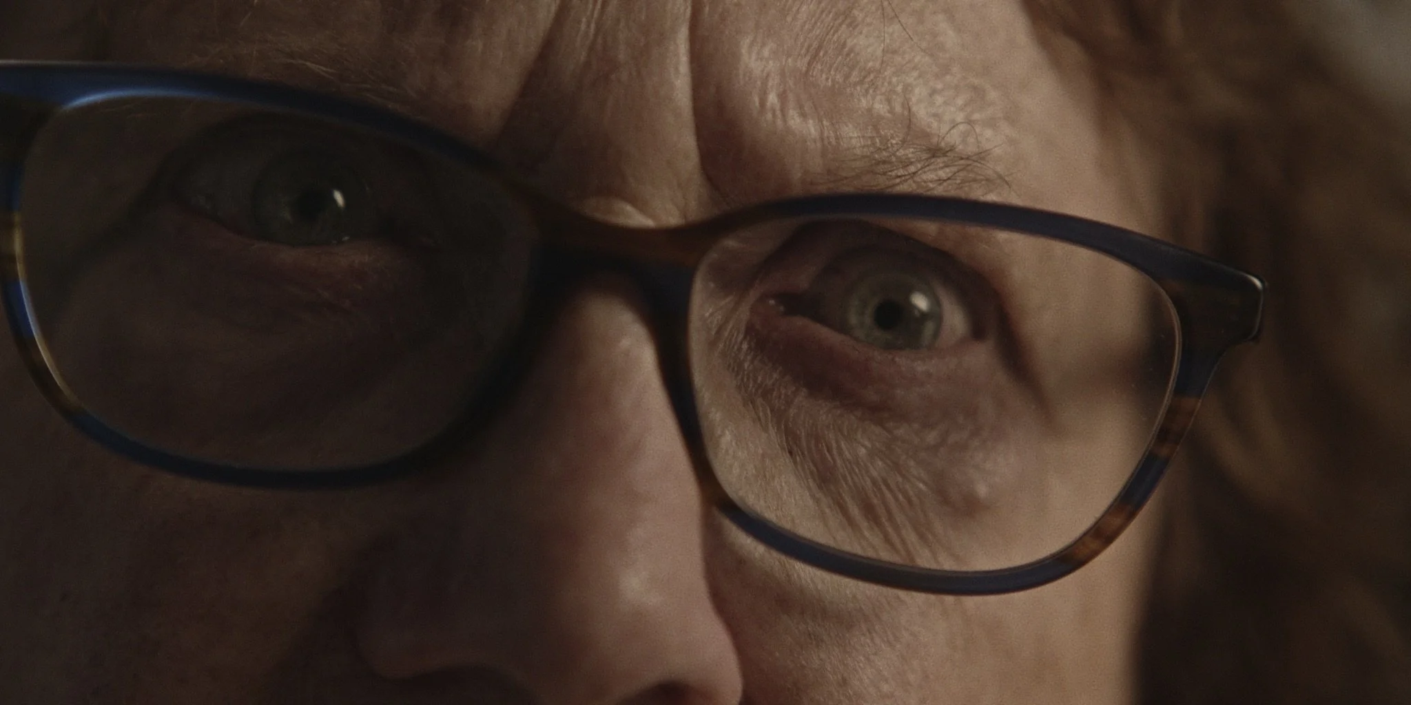 Close-up of a elderly woman's face with glasses, showing hazel eyes and light skin. Actress Yvonne D'Alpra.