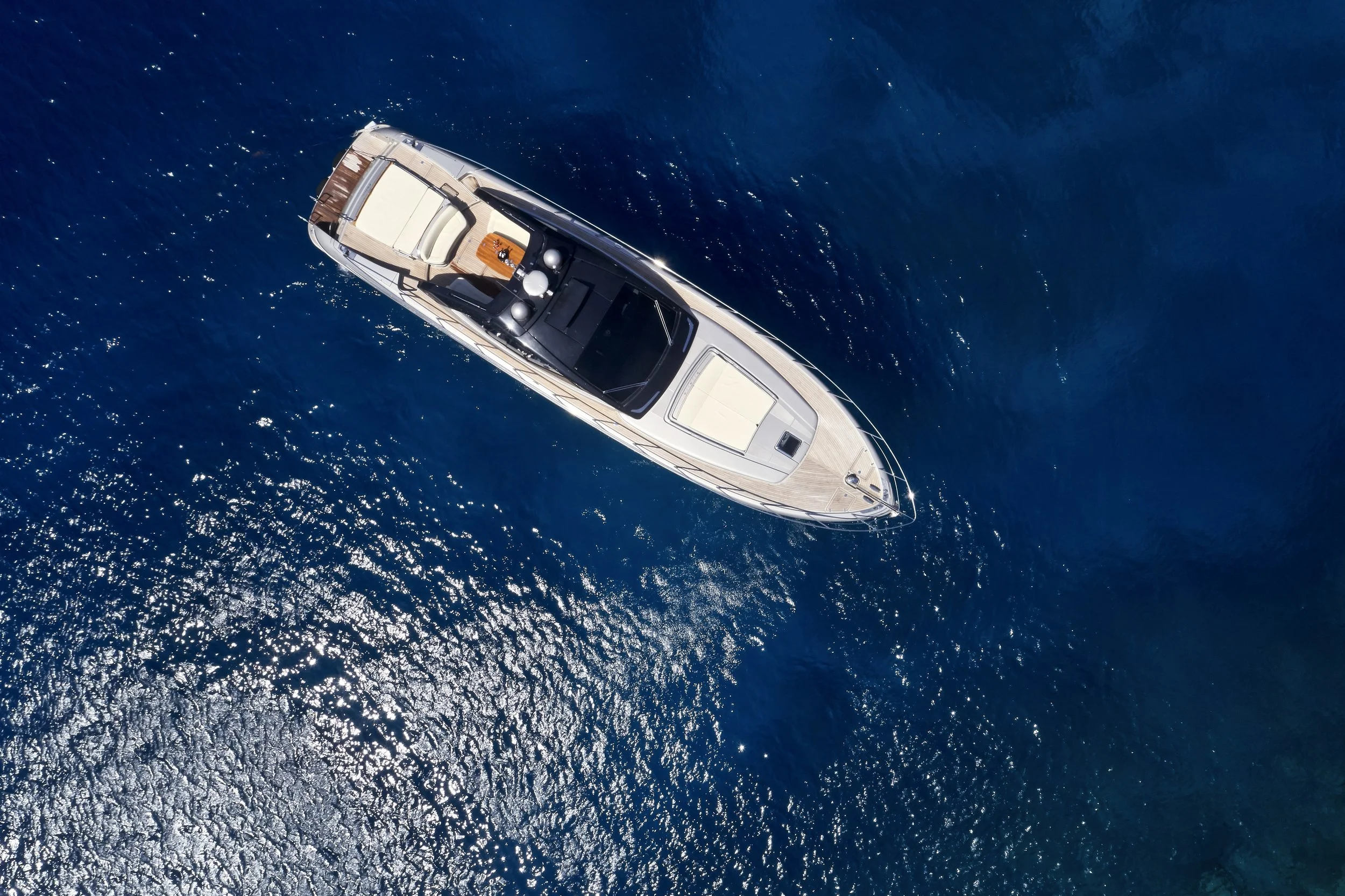 An overhead view of a luxury yacht sailing on deep blue ocean water.