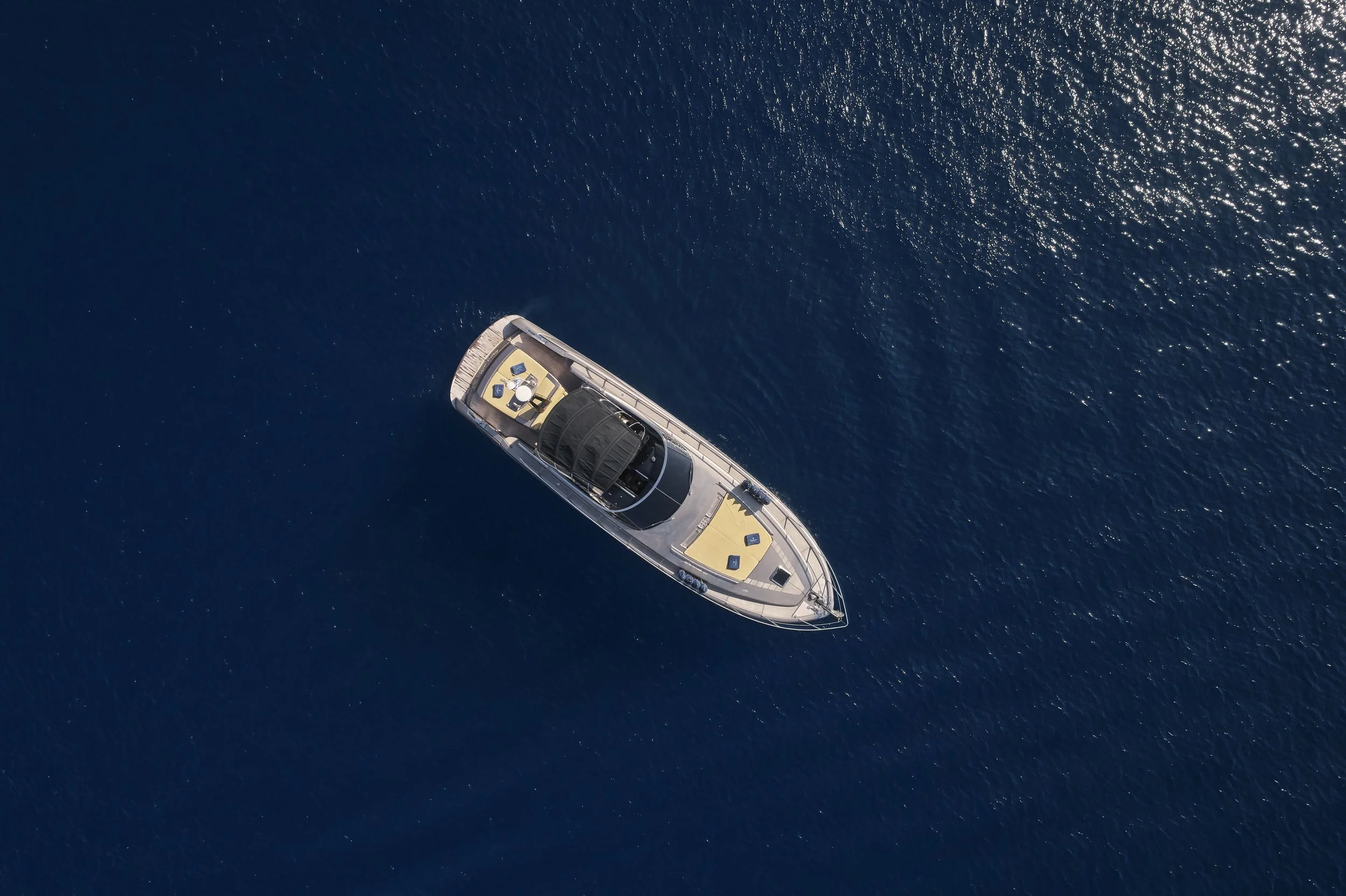 An aerial view of a luxury yacht cruising on deep blue water with sunlight reflections.
