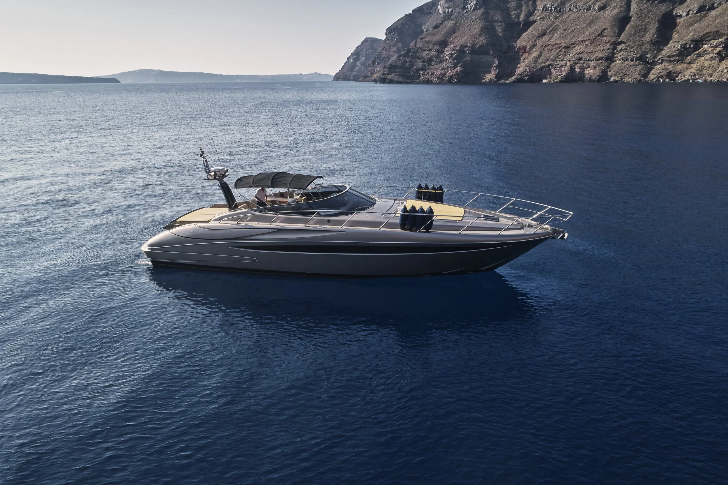 A luxury yacht floating on calm blue water, with a rocky coastline in the background under clear skies.