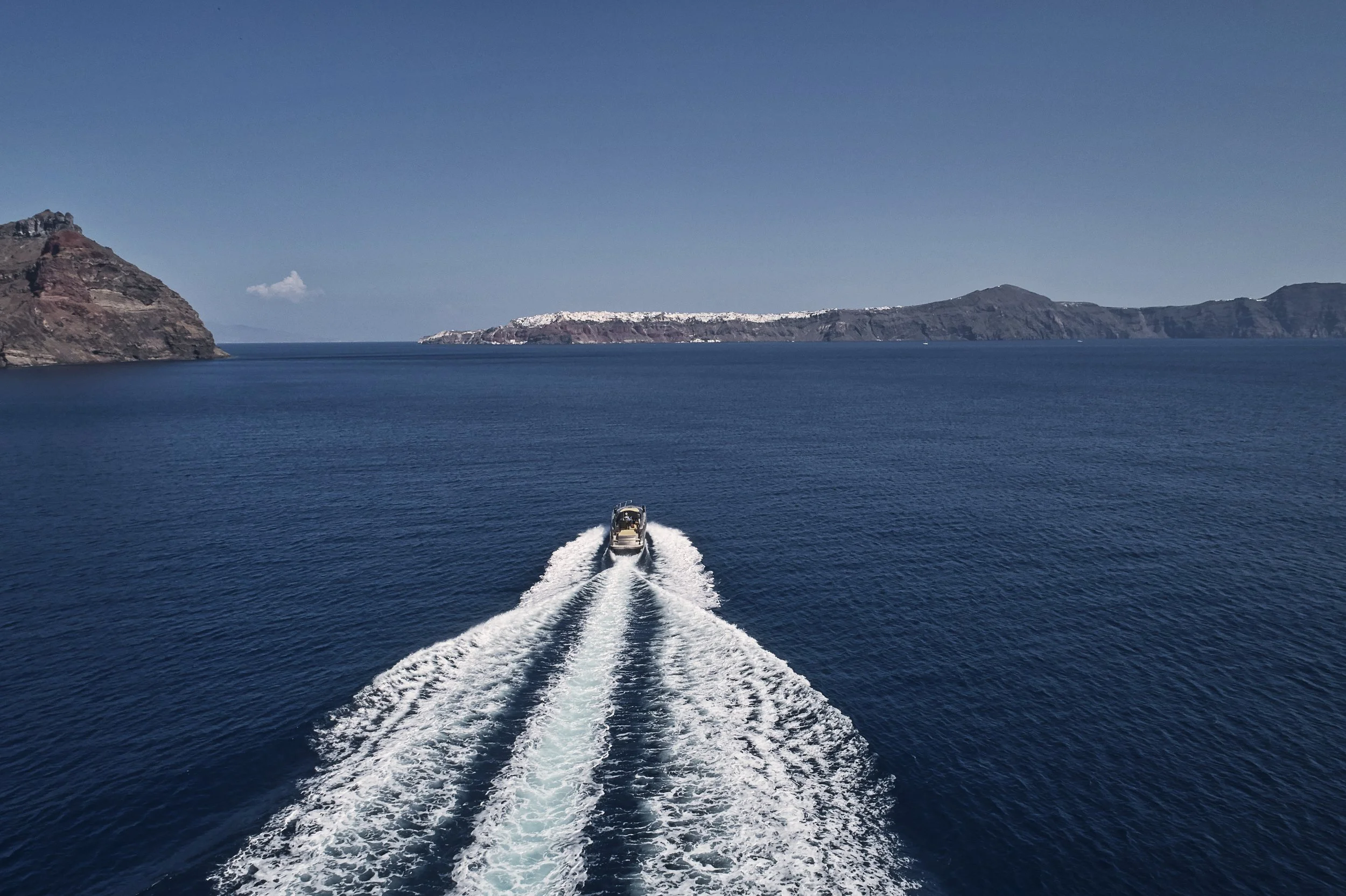 A boat moving through deep blue water with two islands in the background under a clear sky.