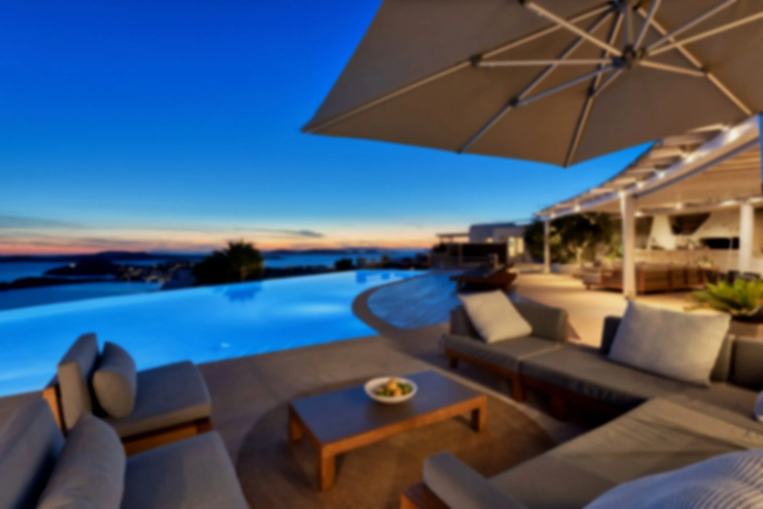 Luxury outdoor living space at sunset with a pool, lounge chairs, large umbrella, and scenic ocean view.