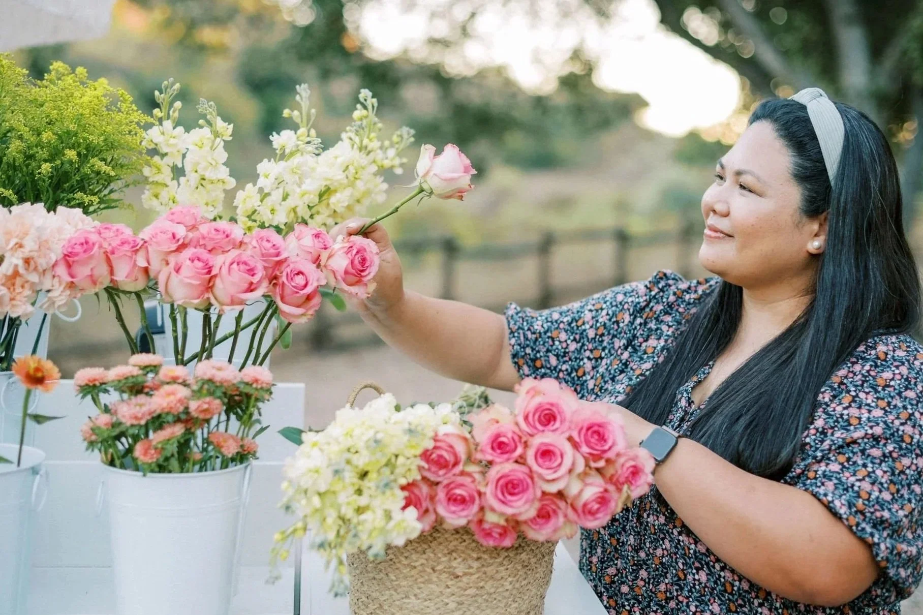 A woman arranging pink and white flowers at an outdoor flower stand.