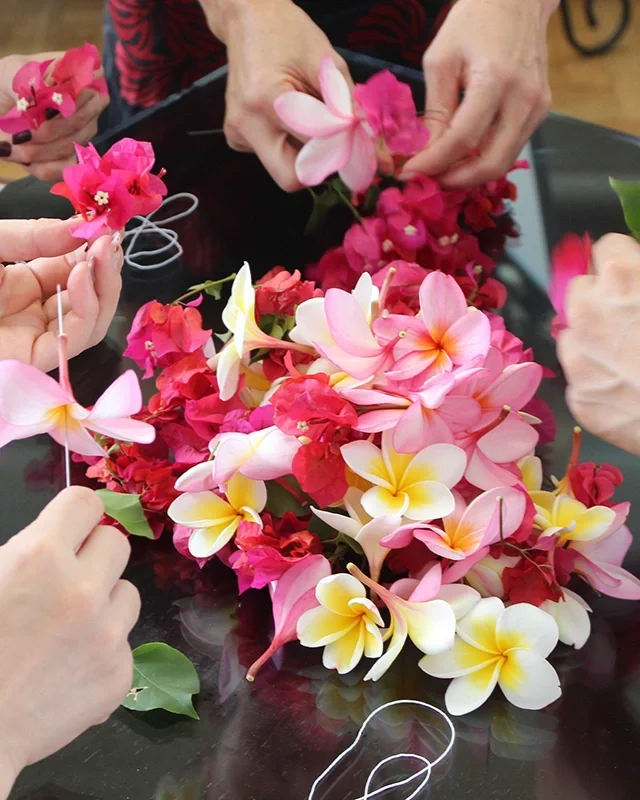 People arranging pink, red, and white flowers, including plumerias and bougainvillea, on a black surface.