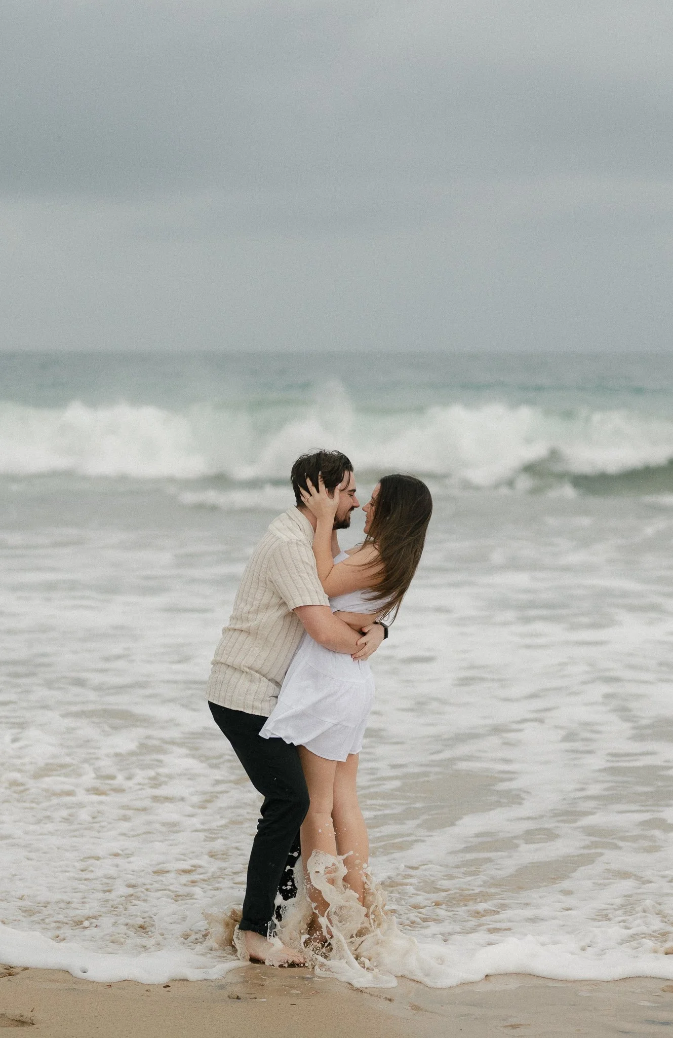 A couple embracing in the ocean waves on a beach, smiling at each other.