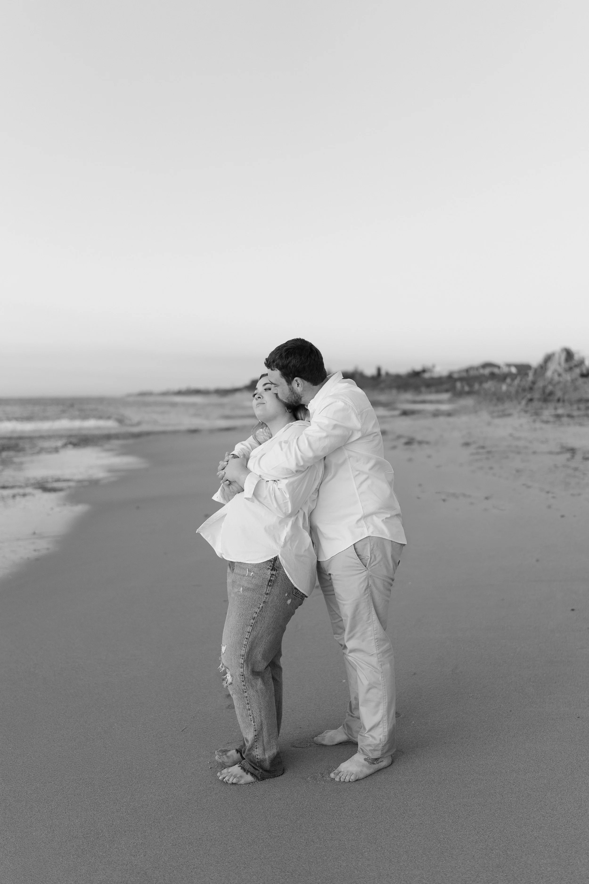A couple standing on the beach, embracing and sharing a kiss by the shoreline.