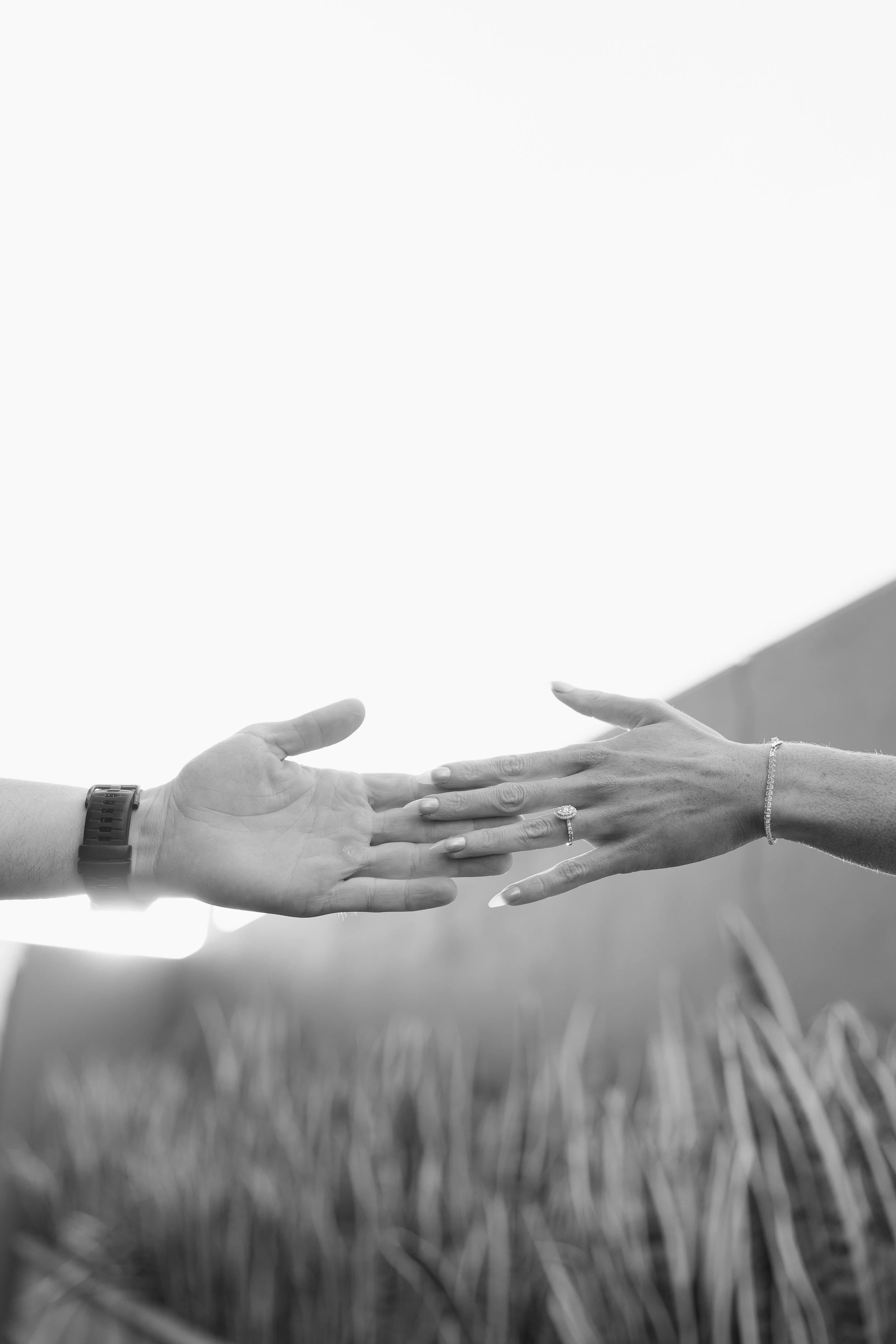 Black and white photo of a man and a woman reaching out to touch each other's hands with a field and building in the background.