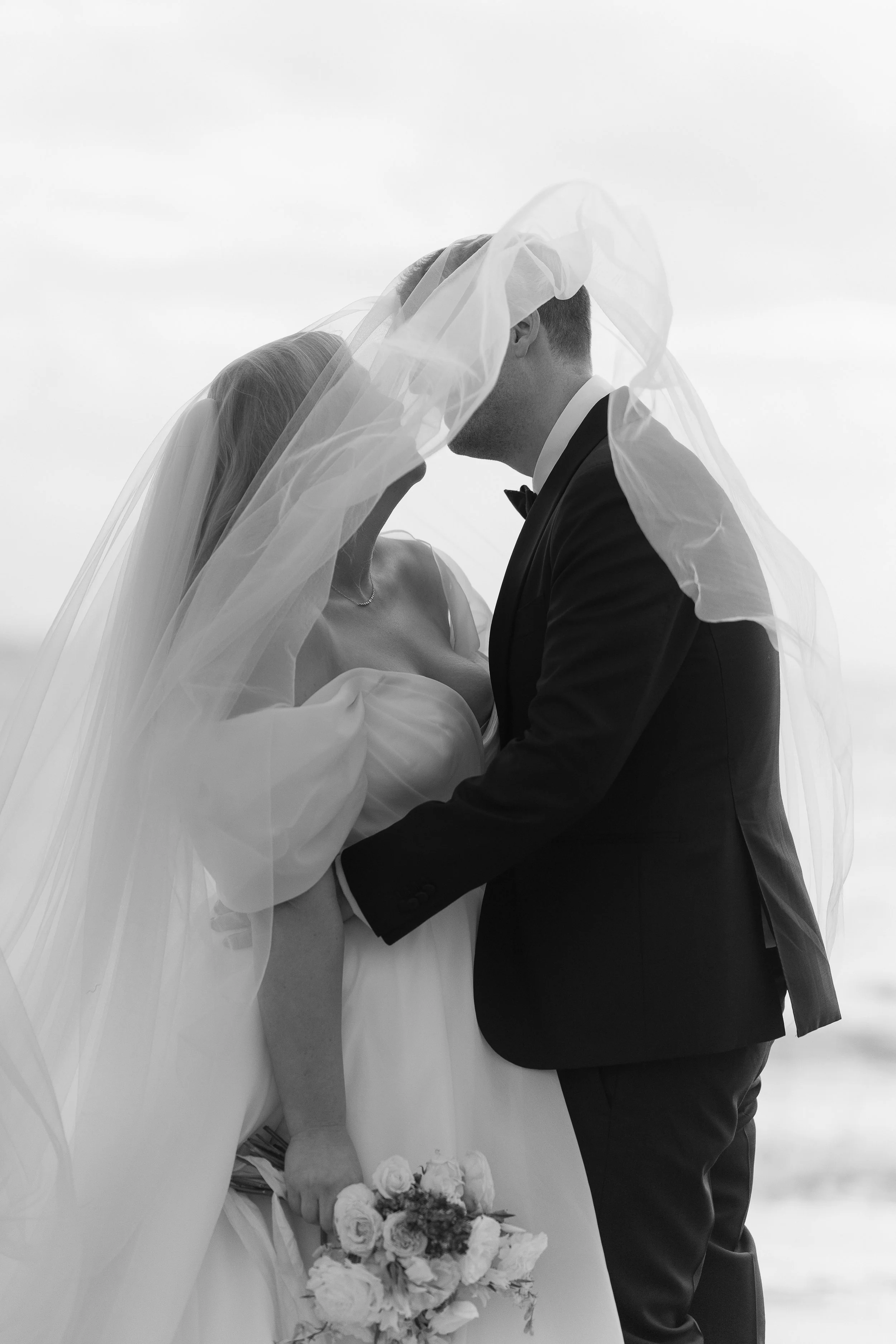 A bride and groom share a kiss under the bride's veil on their wedding day.