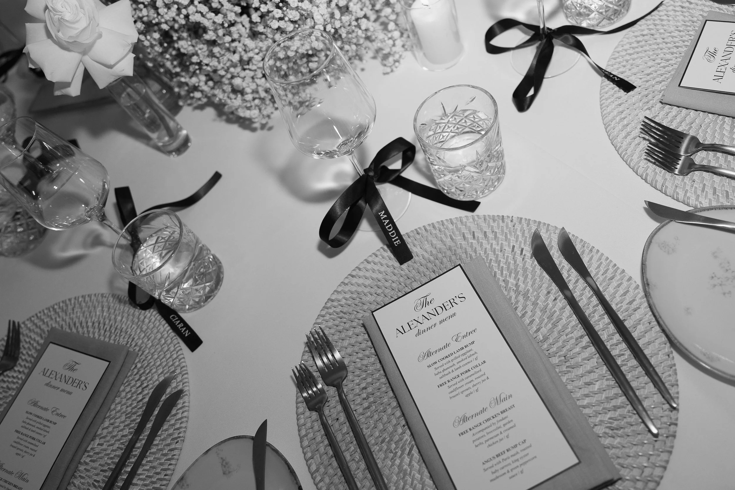A table setup for a formal dinner with place mats, cutlery, glassware, and a printed menu with a floral centerpiece and floating candles.