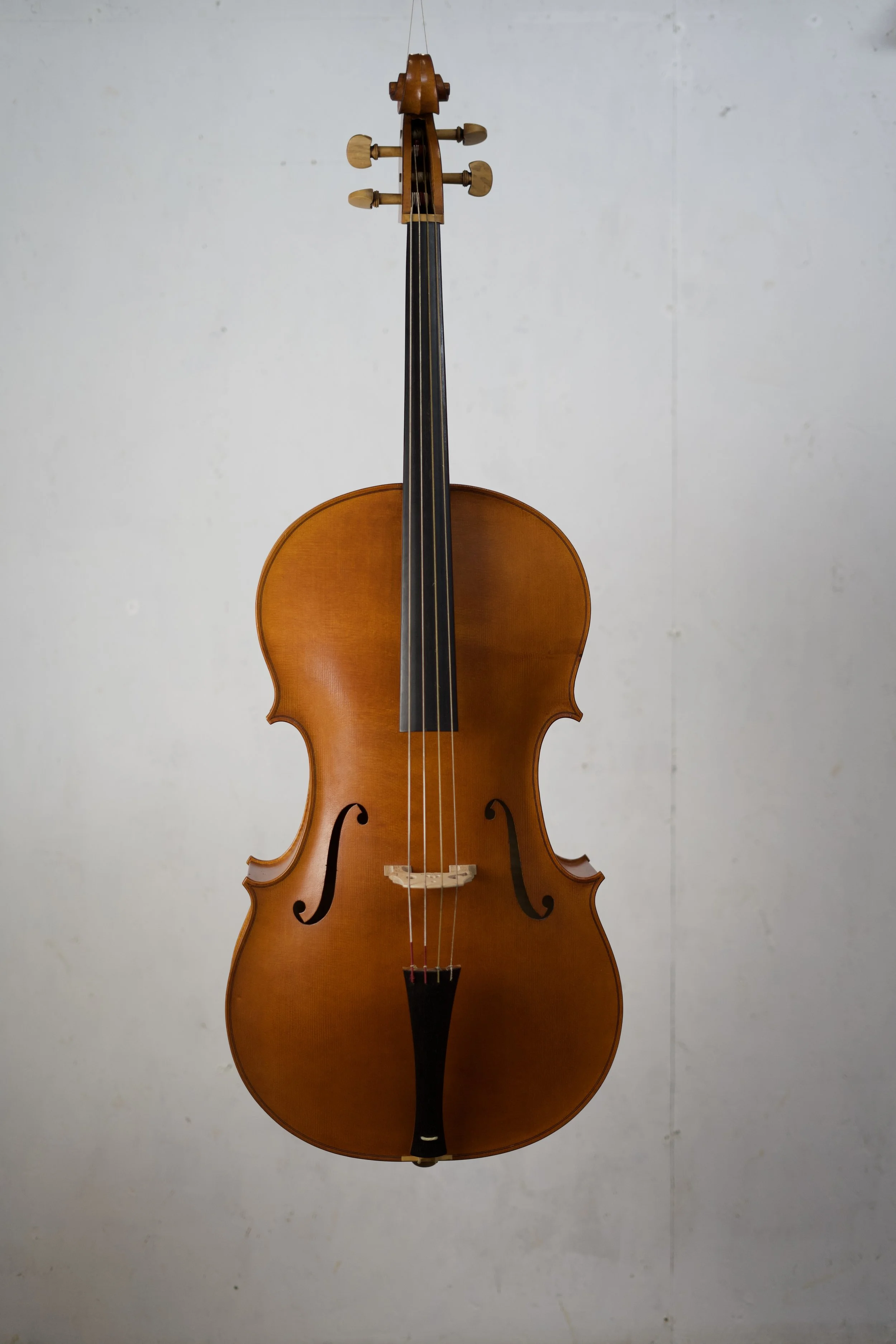 A wooden cello hanging vertically against a plain wall.