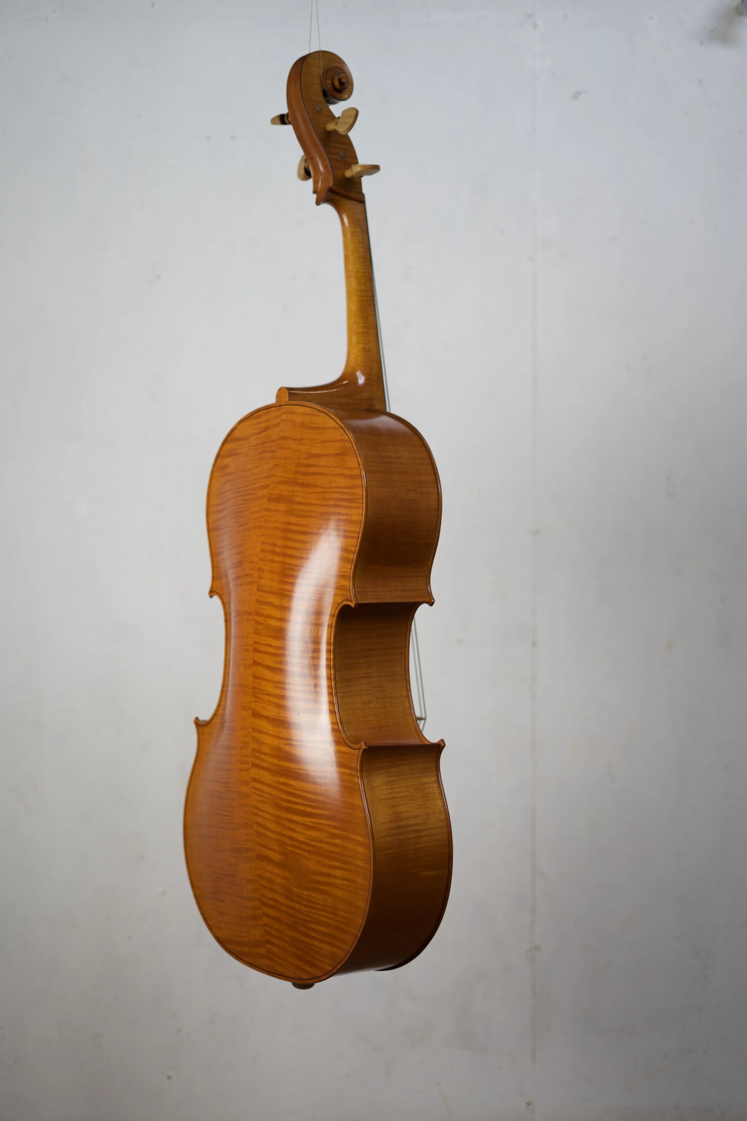A wooden violin hanging vertically against a plain wall.