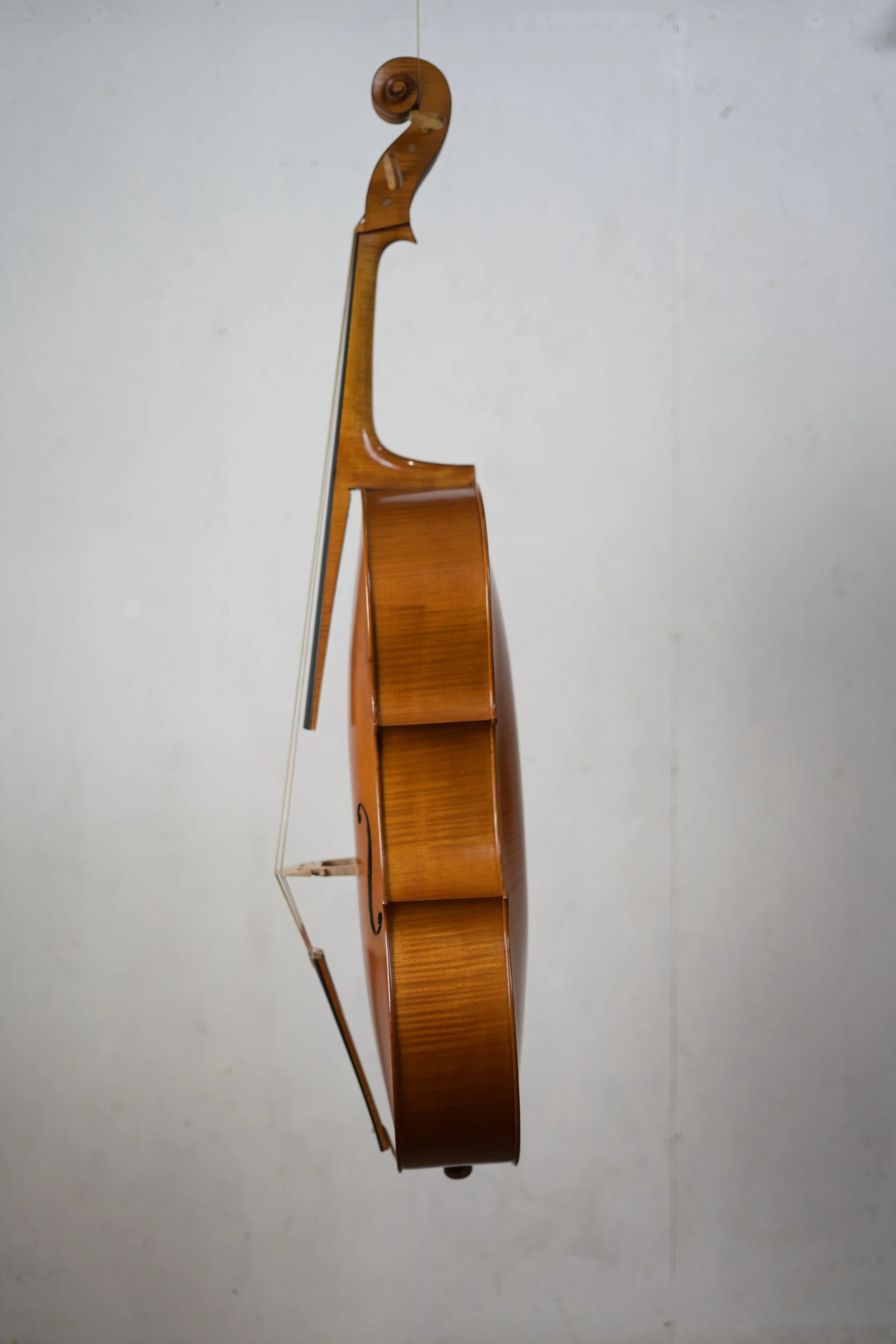 Side view of a wooden cello standing against a plain wall.