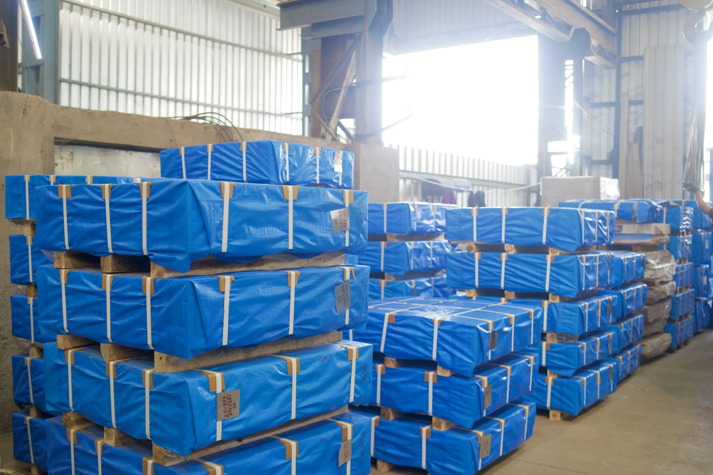 Stacks of wooden pallets wrapped in blue plastic in a warehouse.