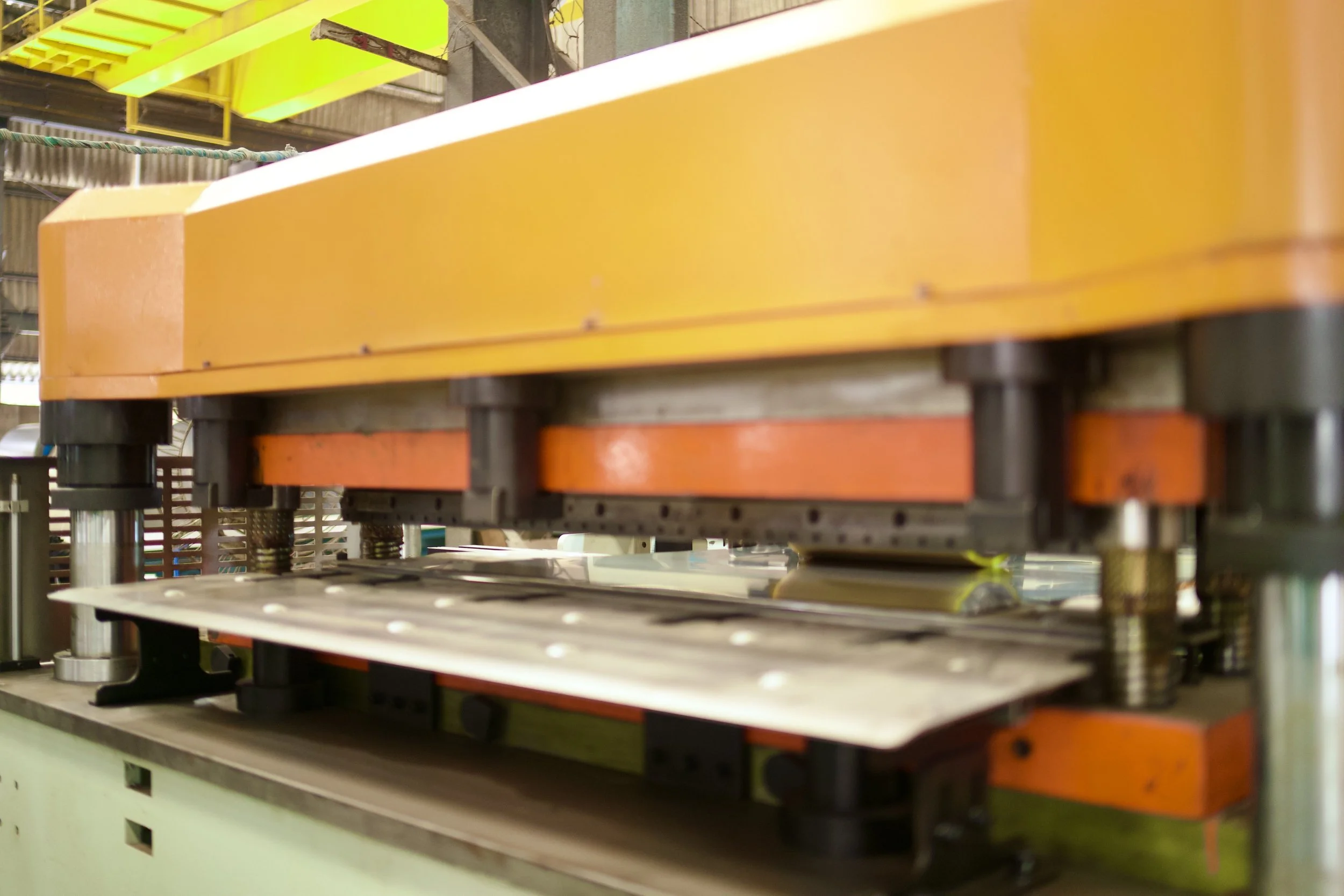 Industrial manufacturing equipment with orange and yellow components and metal parts in a factory setting.