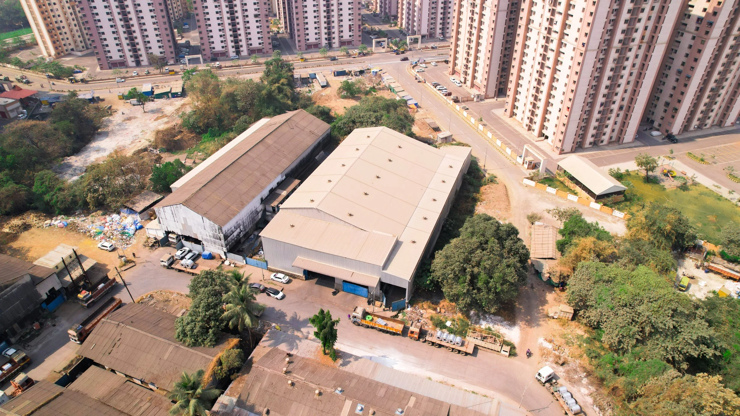 An aerial view of a city block showing high-rise apartment buildings, a large warehouse, a parking lot, some trees, and a construction area.