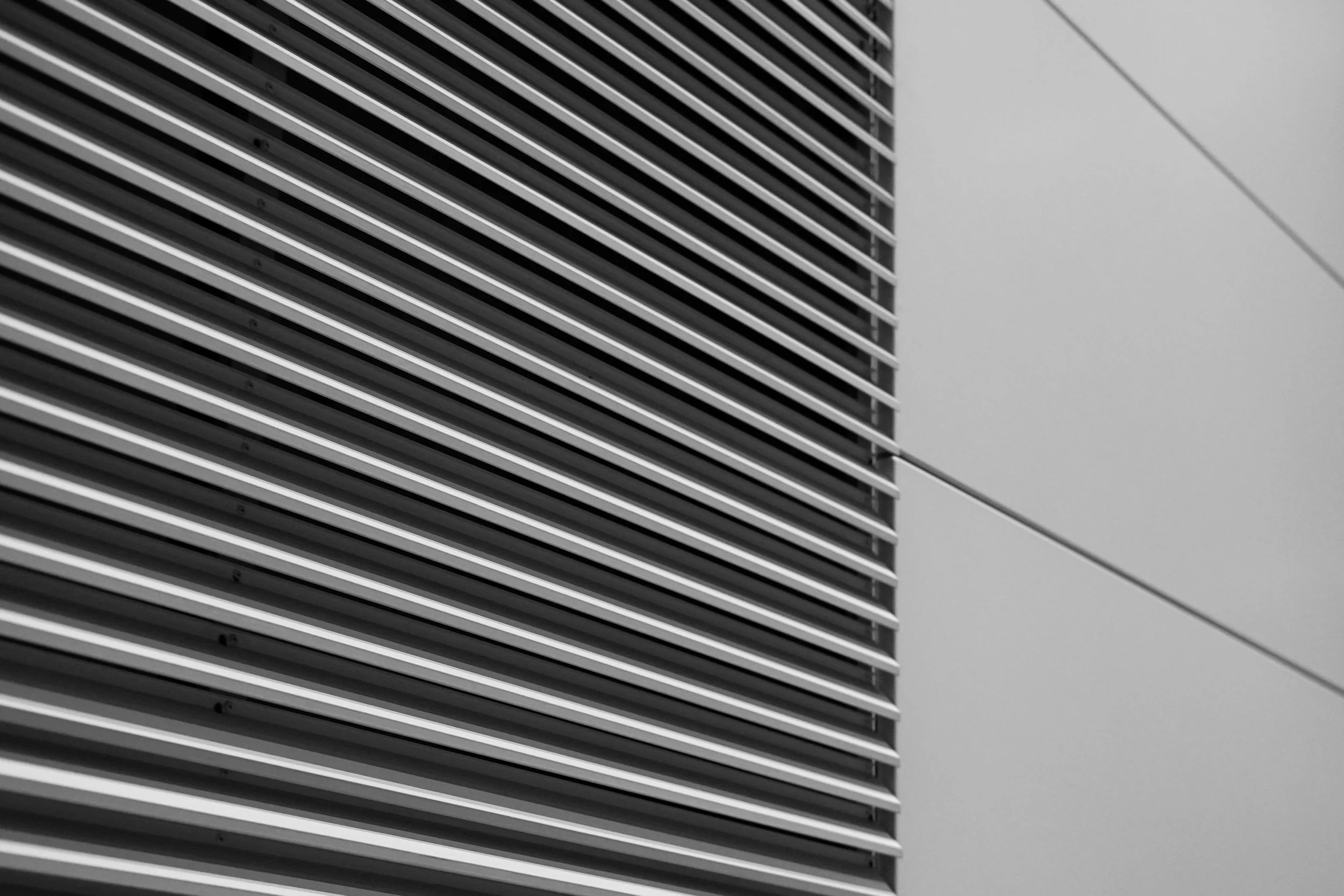 Black and white photo of modern building exterior, showing horizontal metal louvers and smooth wall panels.