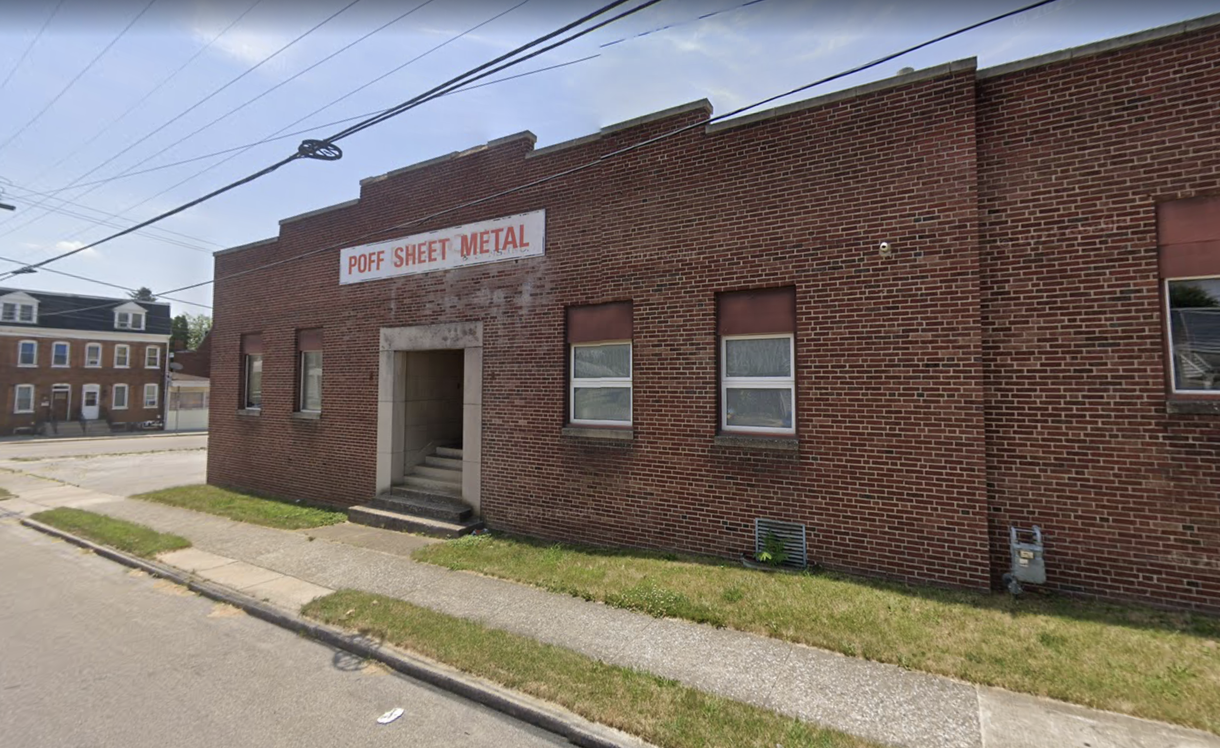 A brick building with a sign that reads 'POFF SHEET METAL' facing a sidewalk on a partly cloudy day.